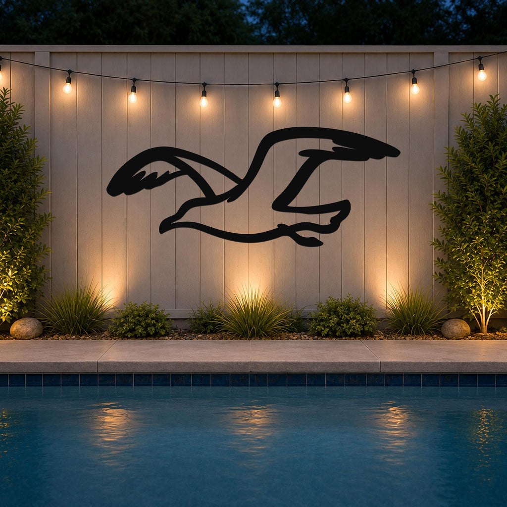 Black metal seagull wall art with motion-line cutouts, mounted on a light-colored outdoor wall above a pool at dusk.