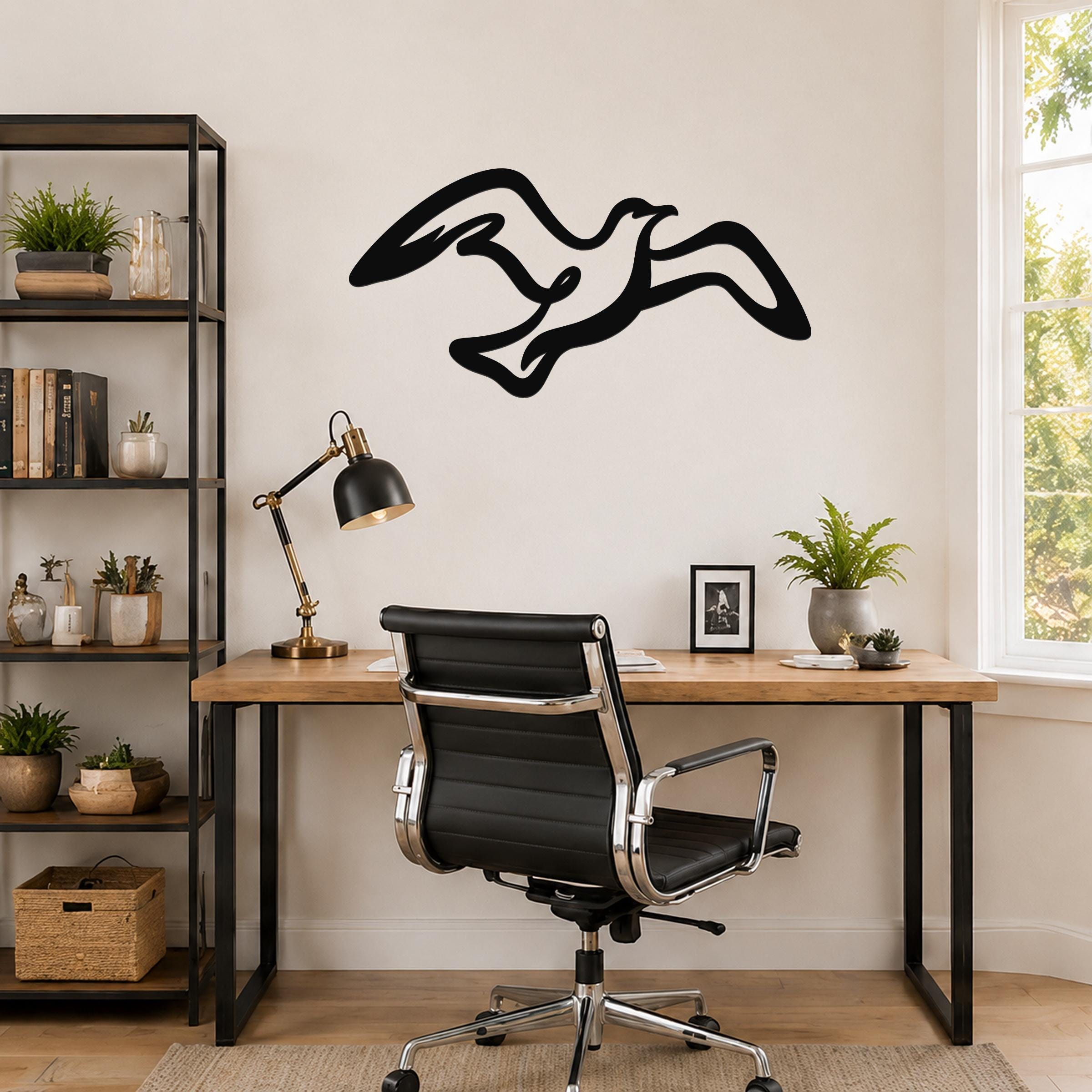 Black metal seagull wall art with flowing wing cutouts, mounted above a wooden desk in a modern home office.