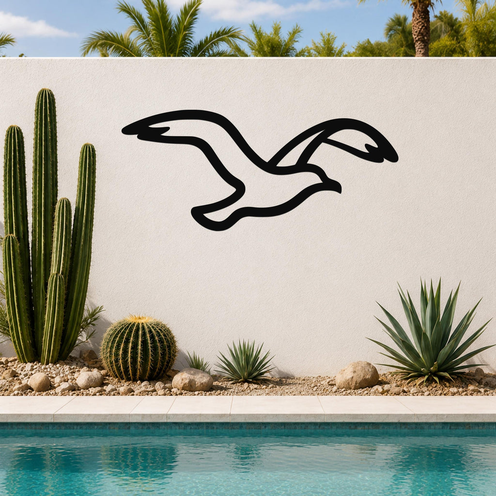 Black metal seagull wall art with a flowing silhouette, mounted on an outdoor wall above a pool with cacti and palm trees in the background.