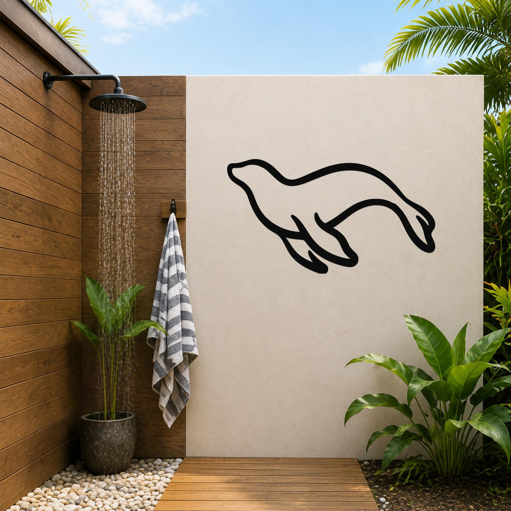 Black metal sea lion wall art silhouette mounted on a beige outdoor wall beside a wooden shower area with a running showerhead and tropical plants.