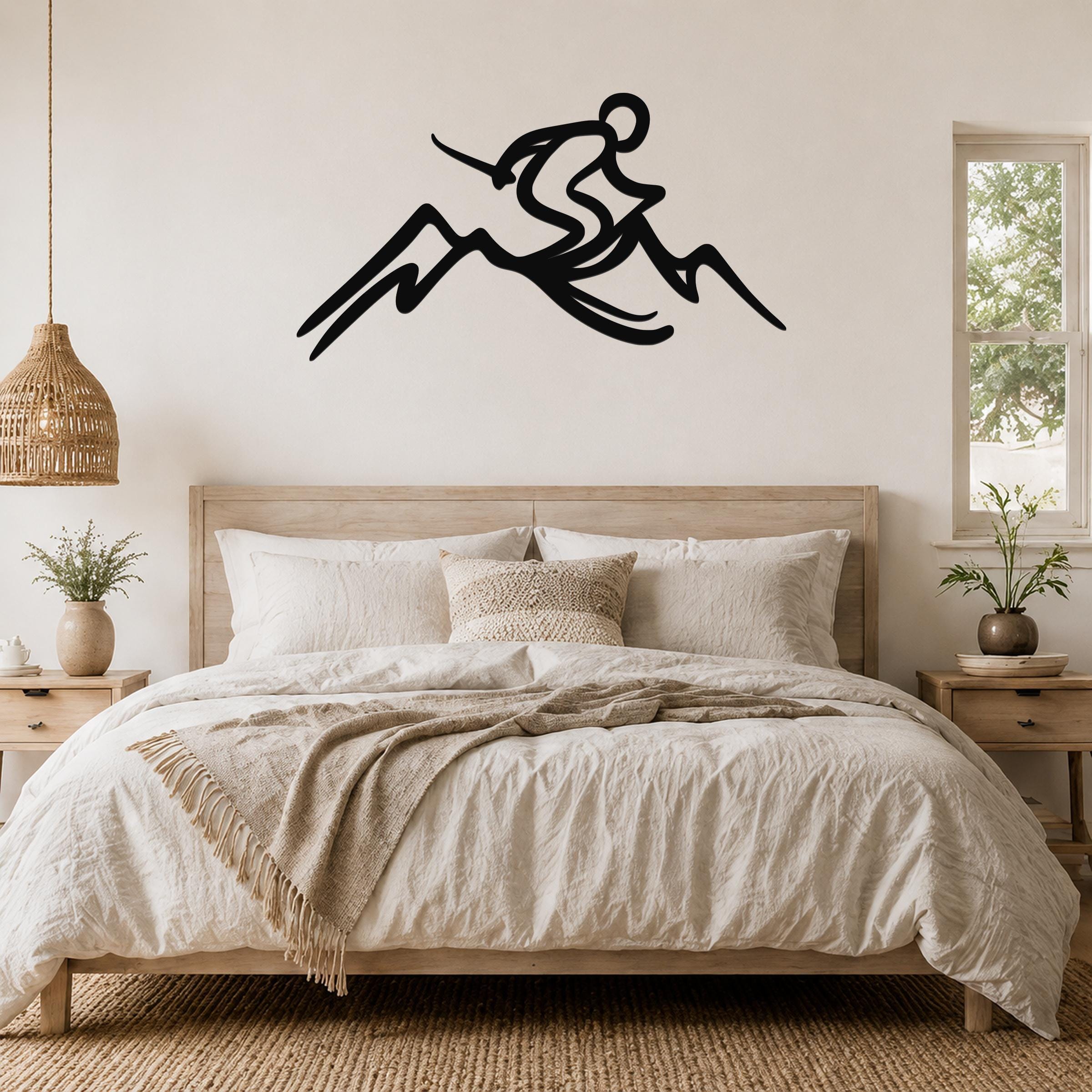 Black metal wall sculpture of a skier in motion above a mountain, mounted on a bedroom wall above a wooden bed.