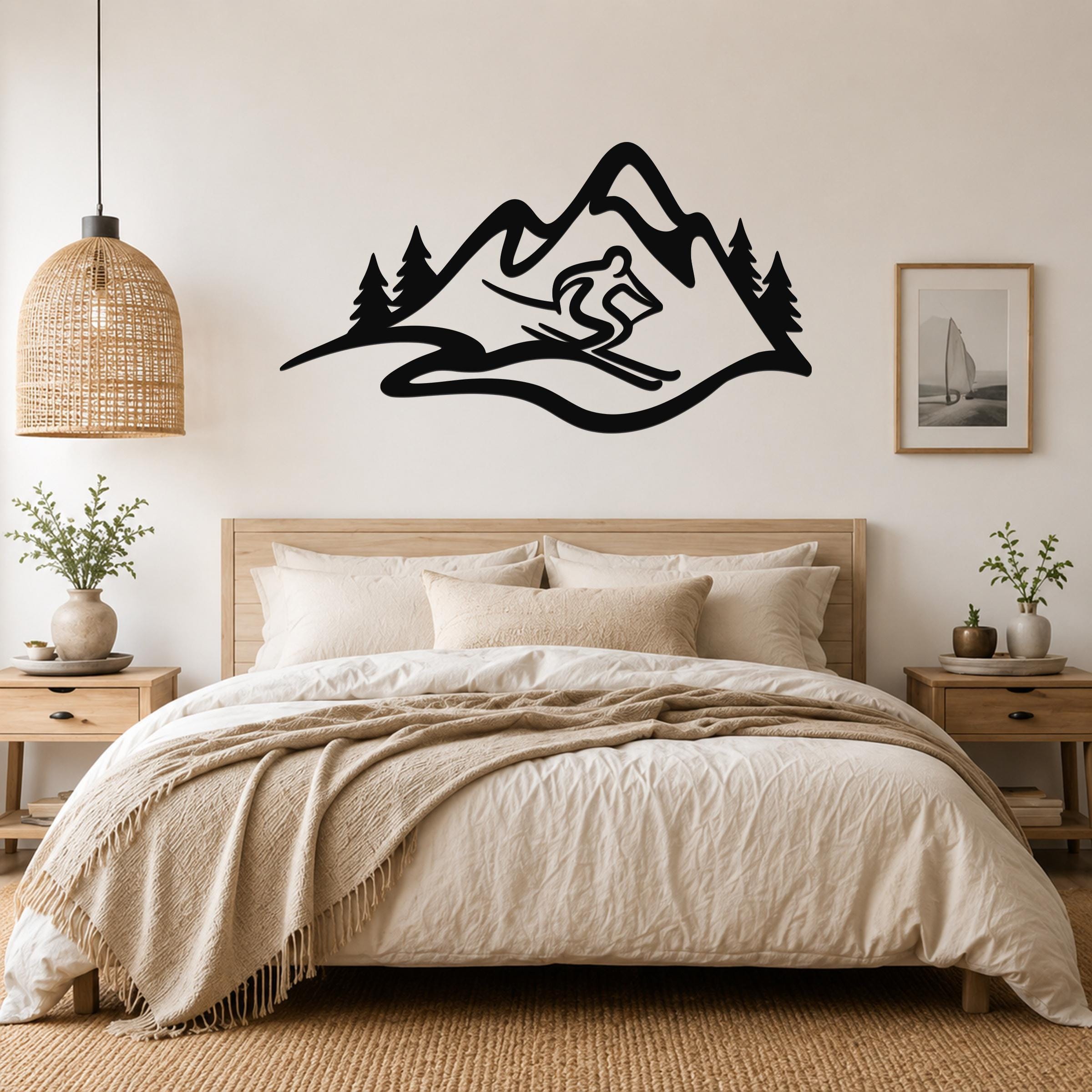 Black metal wall art featuring a skier silhouette and mountain range with pine trees, mounted above a bed in a bedroom.