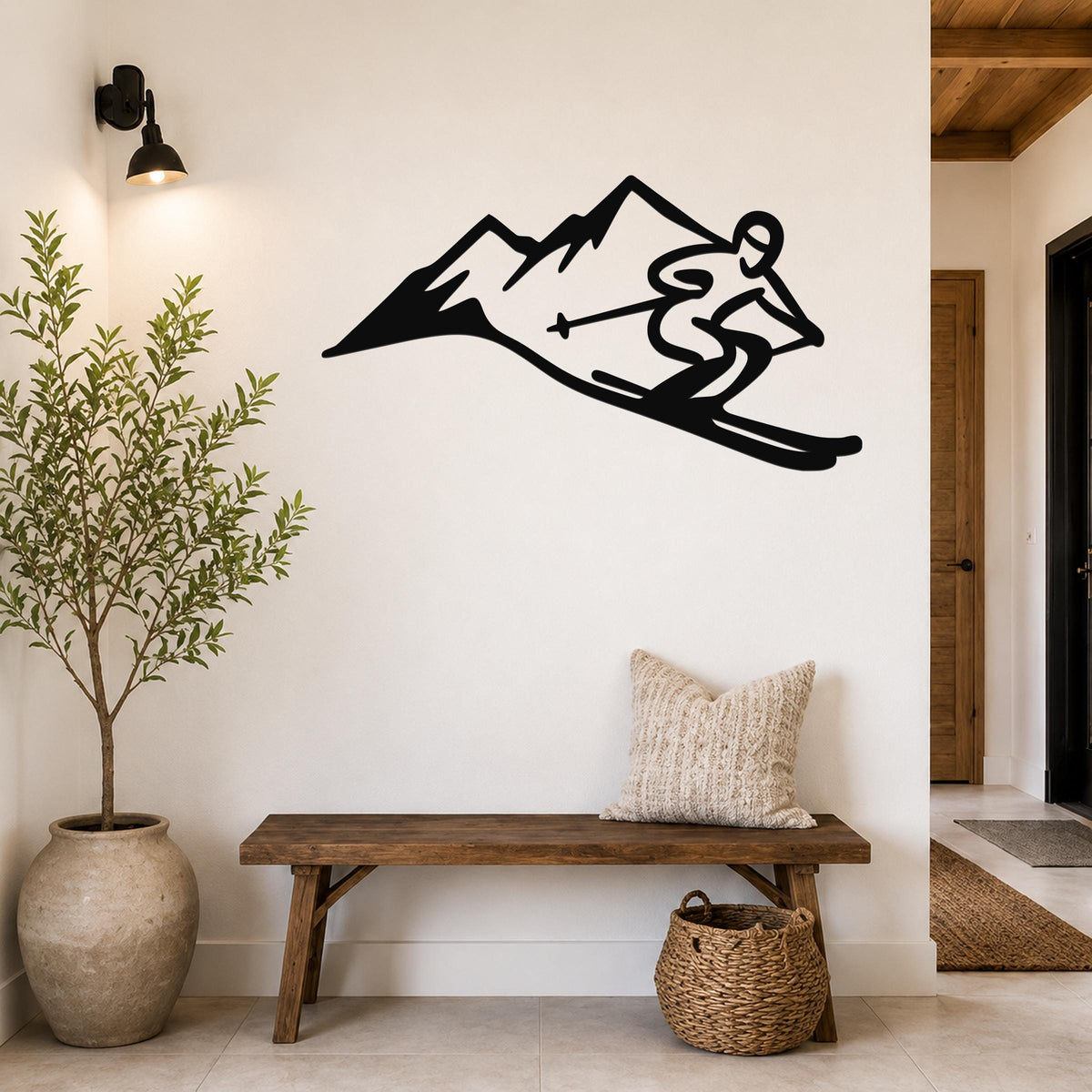 Black metal wall art silhouette of a skier descending a mountain, mounted on a white wall above a wooden bench in a hallway.