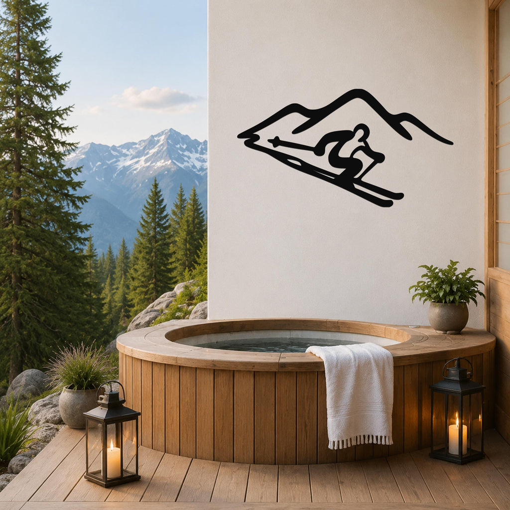 Black metal wall art of a skier silhouette on a mountain slope, mounted on a white wall above a wooden hot tub on a deck with a mountain view.