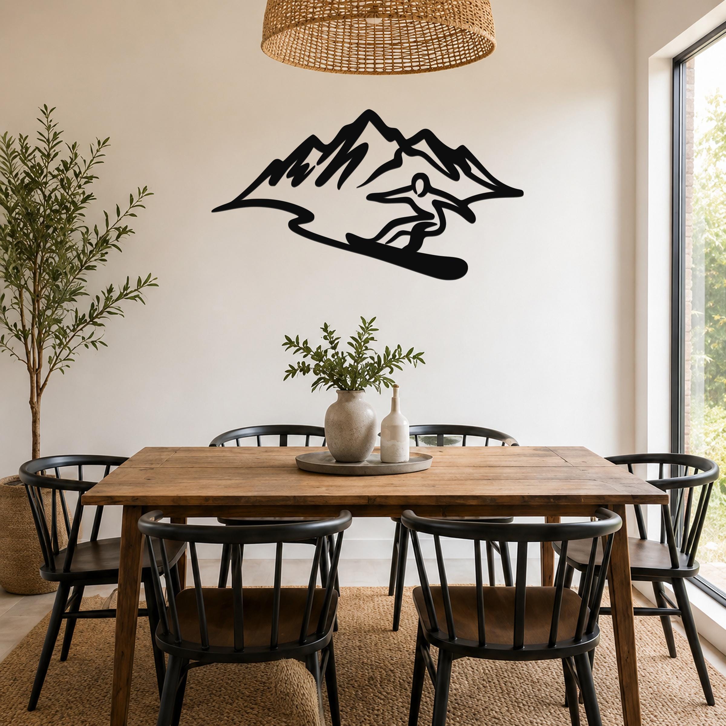 Black metal wall sculpture of a snowboarder in silhouette, mounted on a dining room wall above a wooden table.