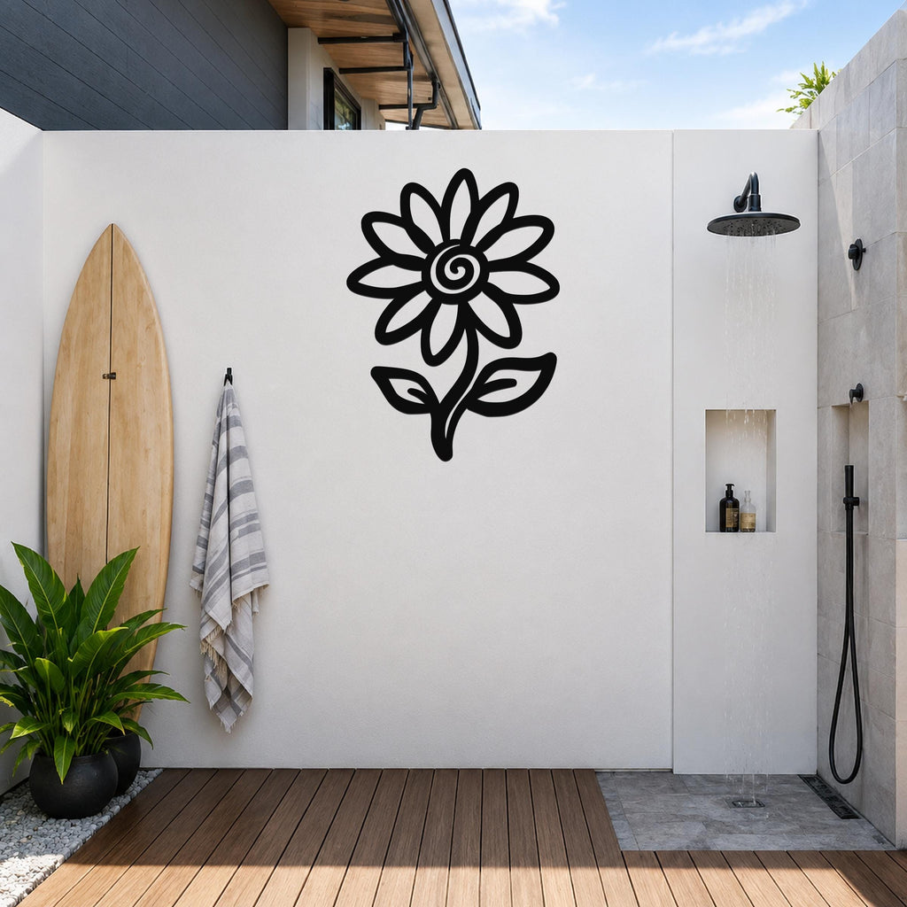 Black metal sunflower wall art silhouette with spiral center and leaves, mounted on a white outdoor wall above a wooden deck near a shower area.