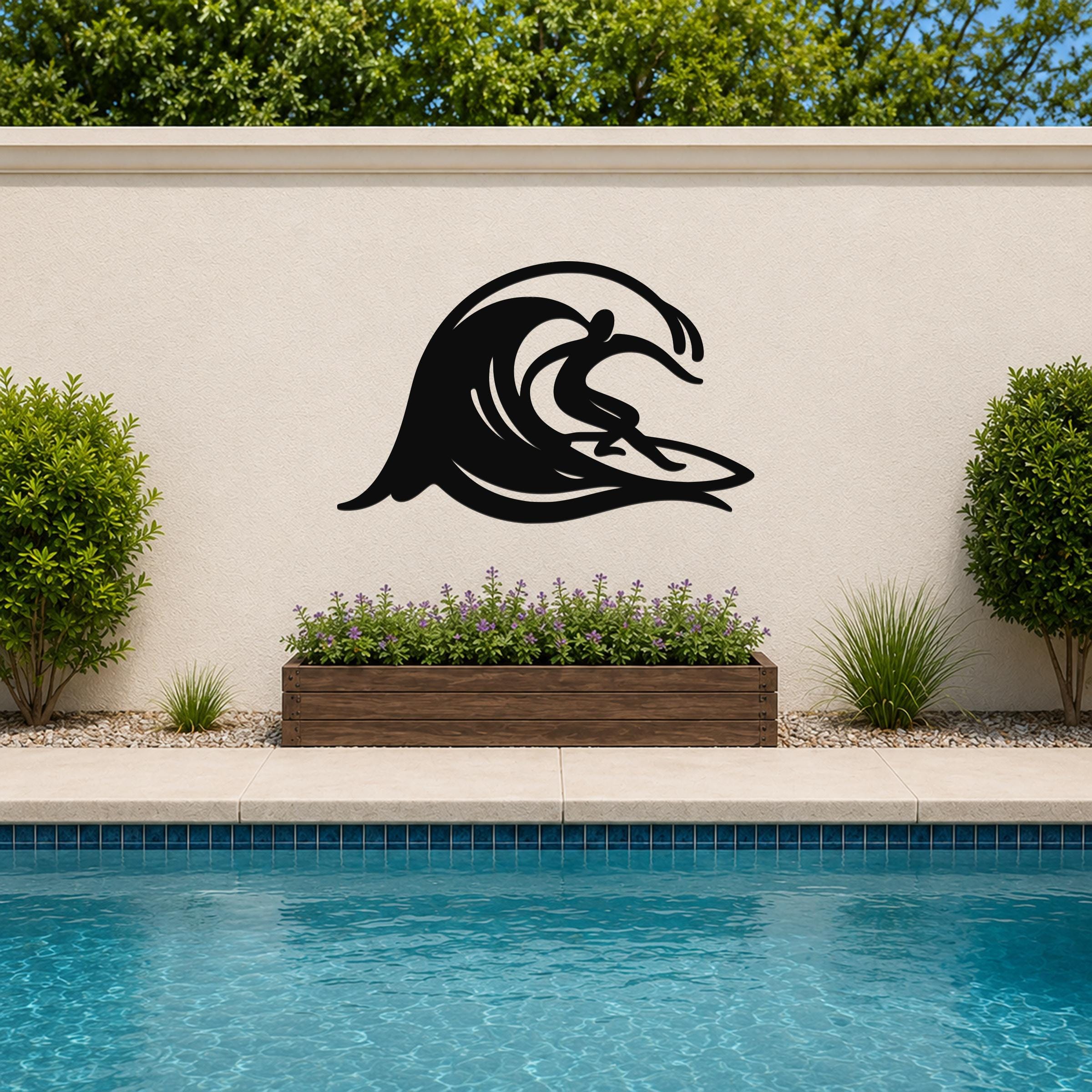 Black metal wall art in a surfer riding a wave silhouette, mounted on an outdoor wall above a planter and pool.