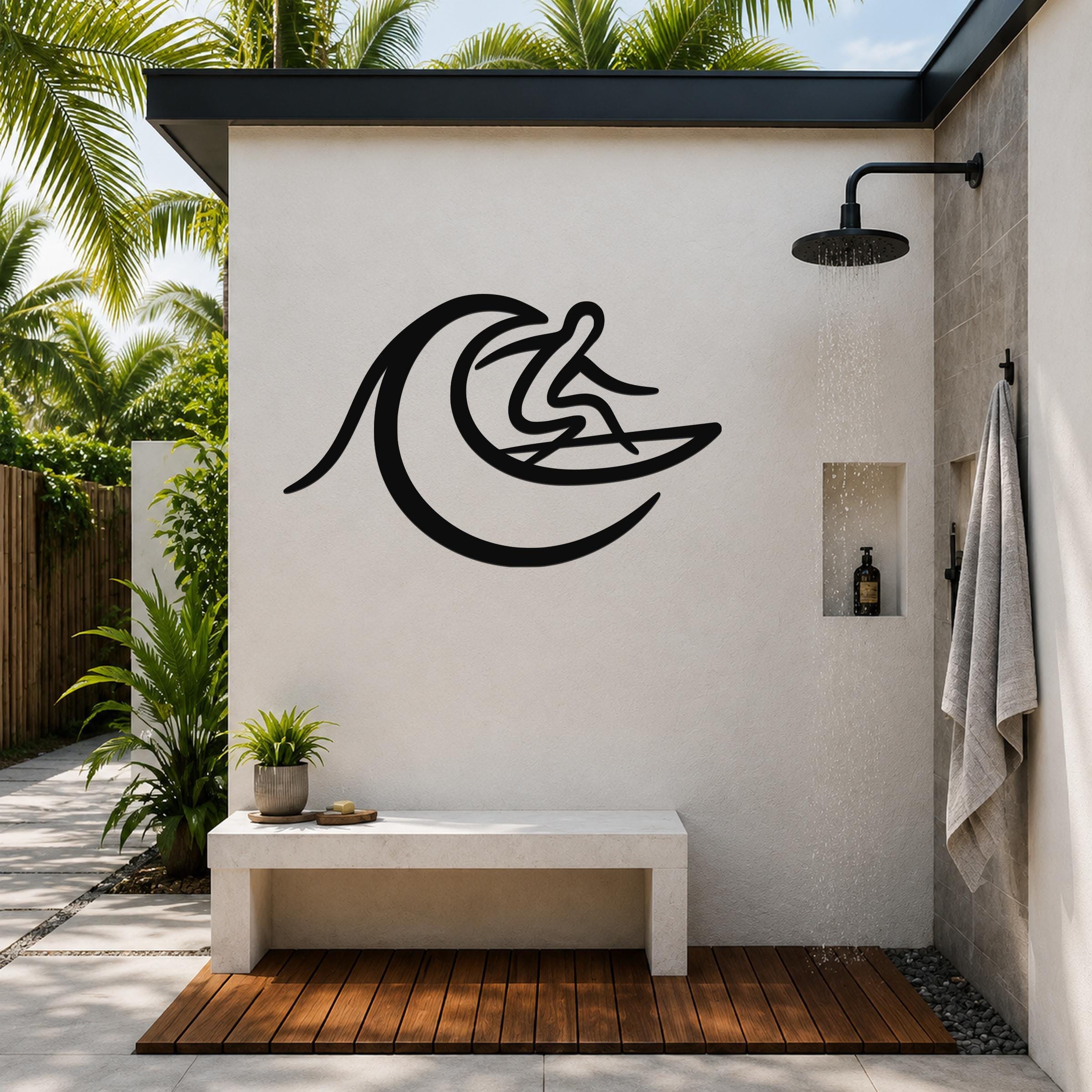 Black metal surfer wall art with wave cutout, mounted on an outdoor shower wall above a bench in a tropical patio setting.