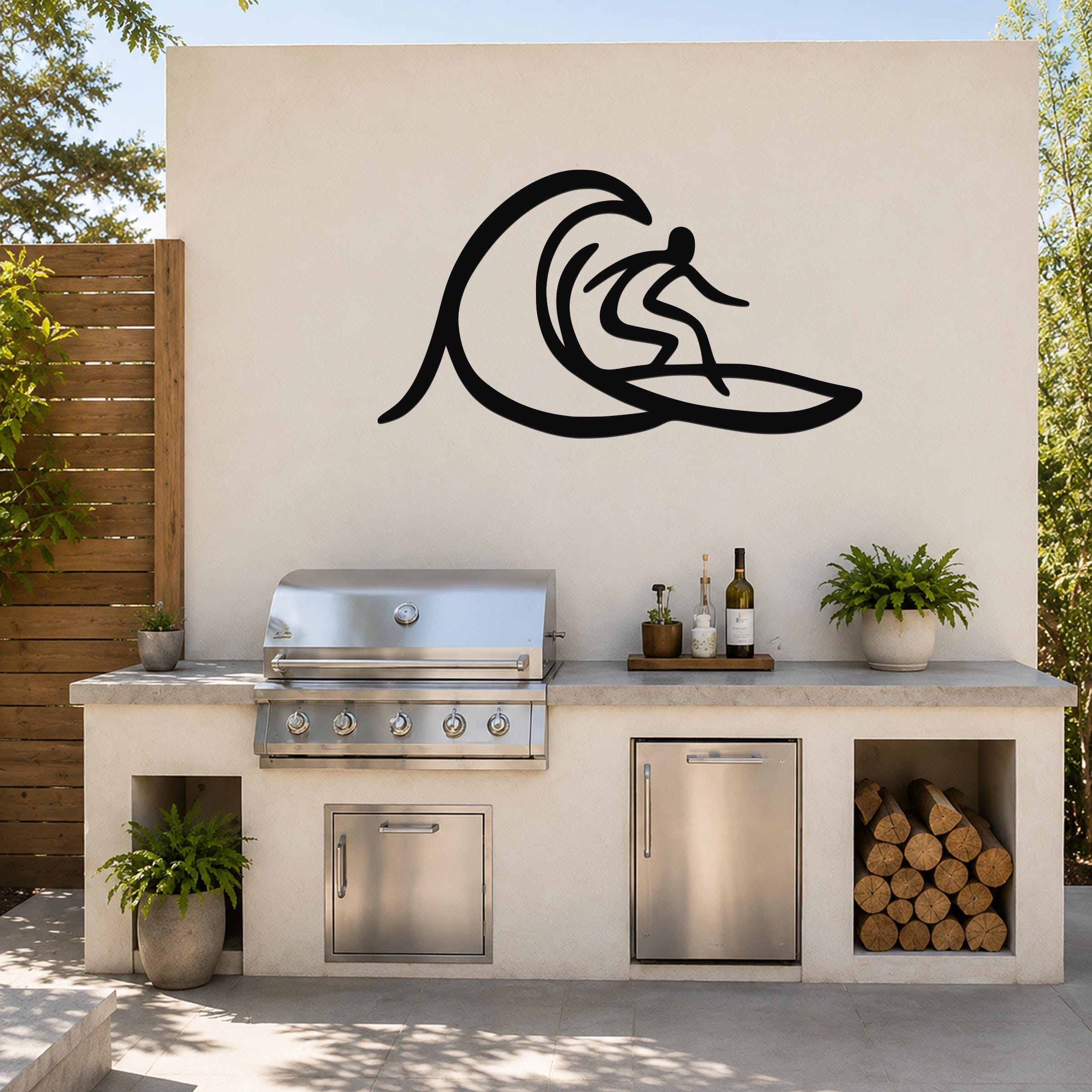 Black metal surfer wall art with wave silhouette, mounted on an outdoor kitchen wall above a stainless steel grill and counter.