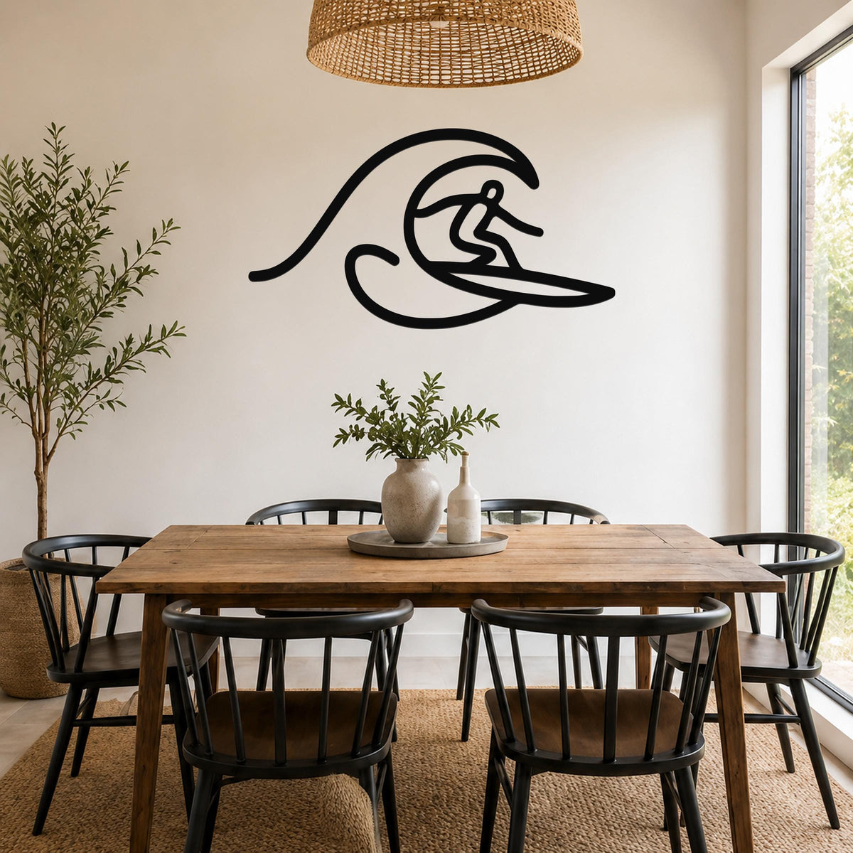 Black metal surfer wall art with flowing wave cutout, mounted on a white wall above a wooden dining table in a bright room.