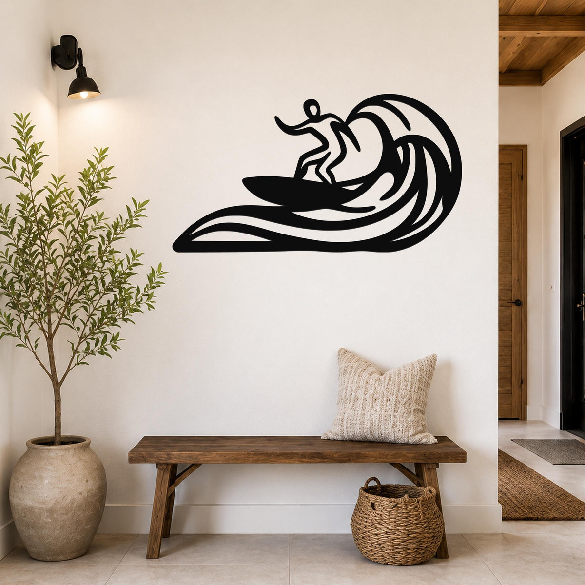 Black metal surfer wall art with wave cutouts, mounted on a white wall above a wooden bench in a hallway.