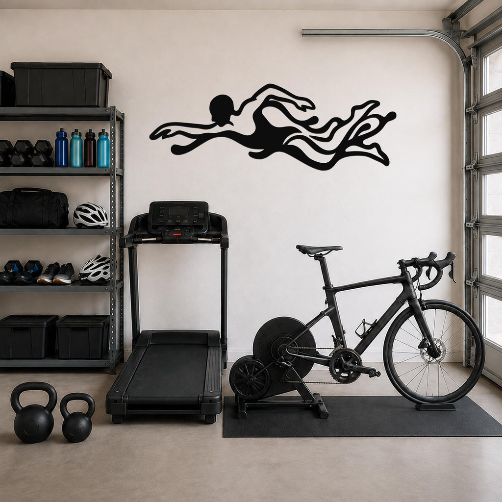 Black metal swimmer wall art with flowing motion cutouts, mounted on a garage wall above a treadmill and exercise bike.