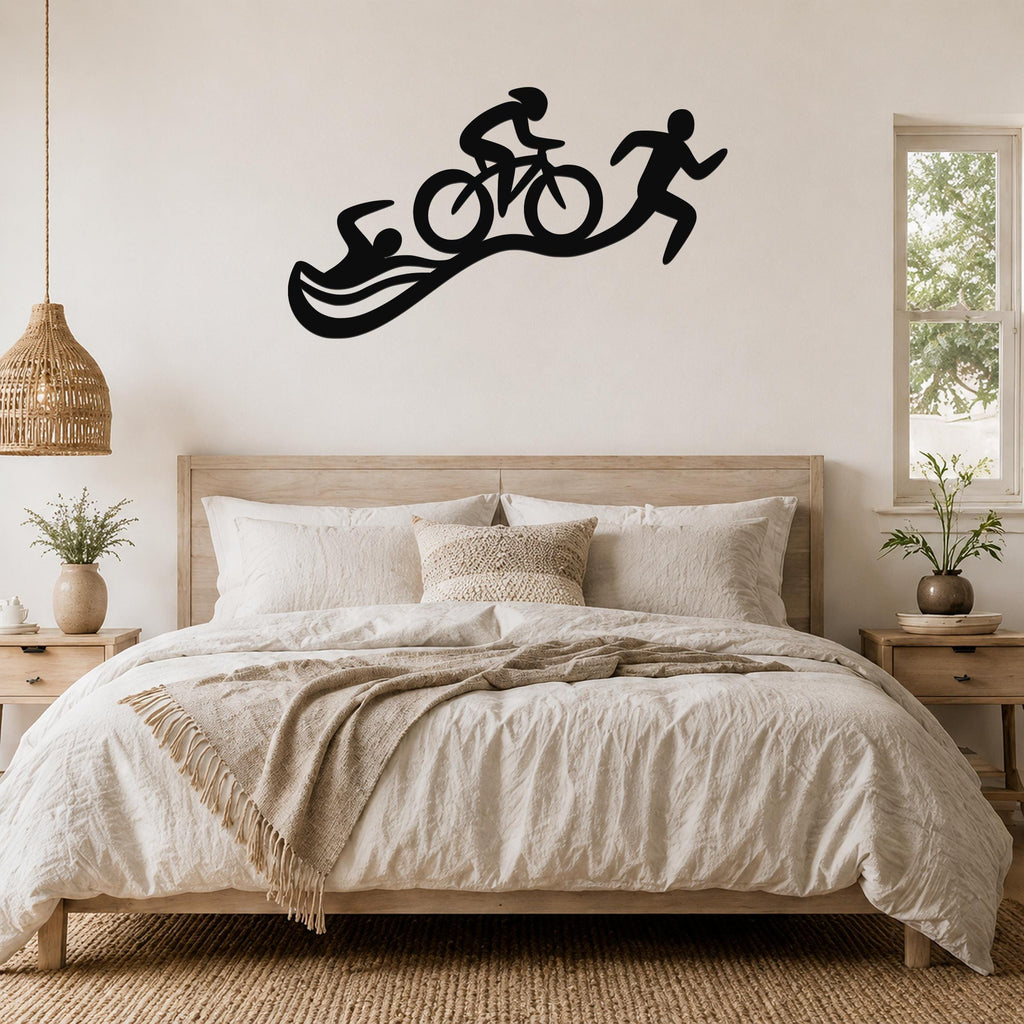 Black metal triathlon wall art with swim, bike, and run silhouettes, mounted above a bed in a neutral bedroom.
