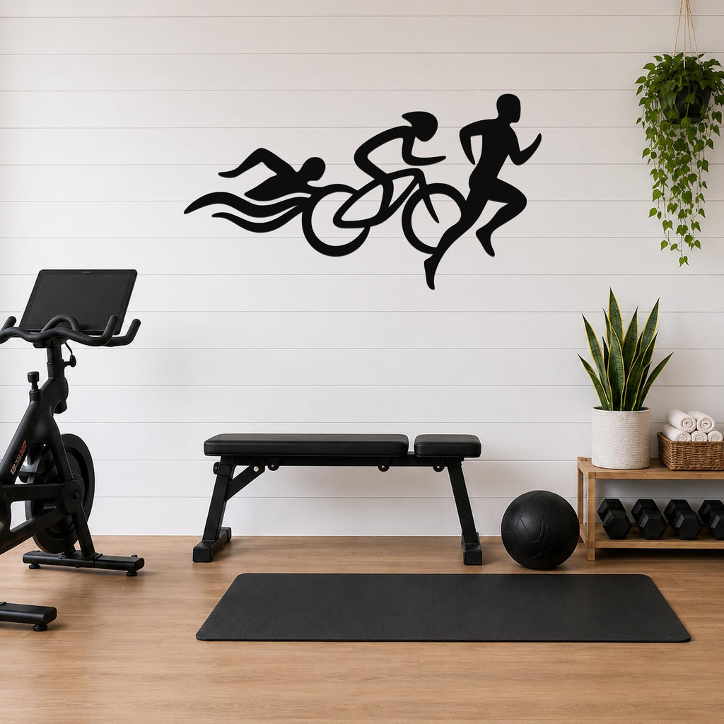 Black metal triathlon wall art with swim, bike, and run silhouettes and motion lines, mounted on a white shiplap wall above a workout bench in a home gym.
