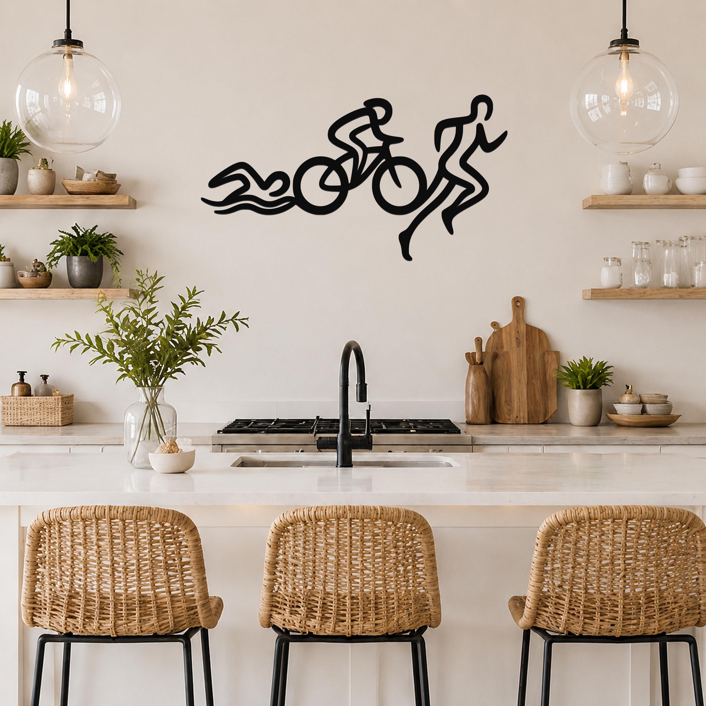 Black metal triathlon wall art with swim, bike, and run silhouette cutouts, mounted above a kitchen counter.