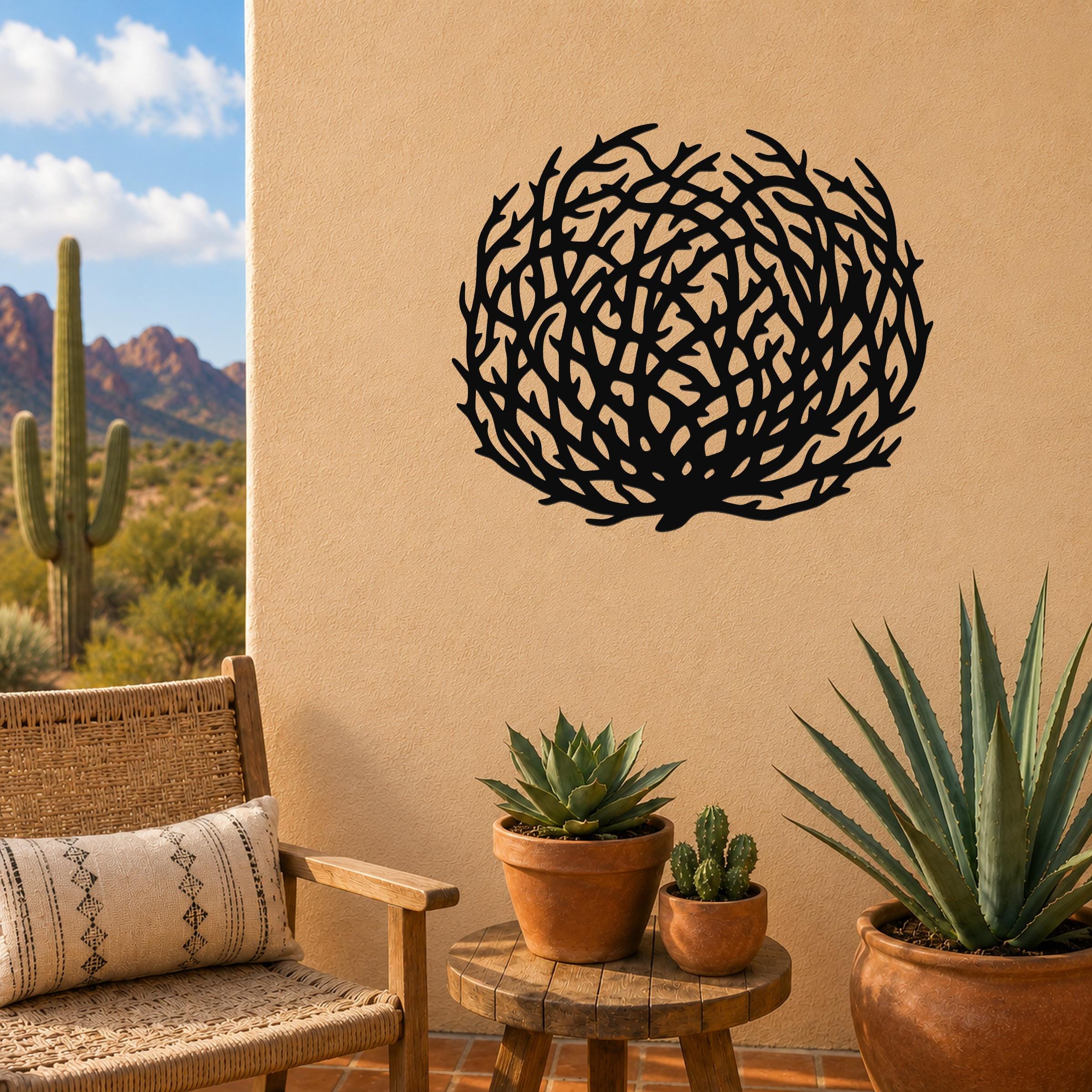 Black metal tumbleweed wall art with intricate branch cutouts, mounted on a tan outdoor wall above a small wooden table with potted succulents.