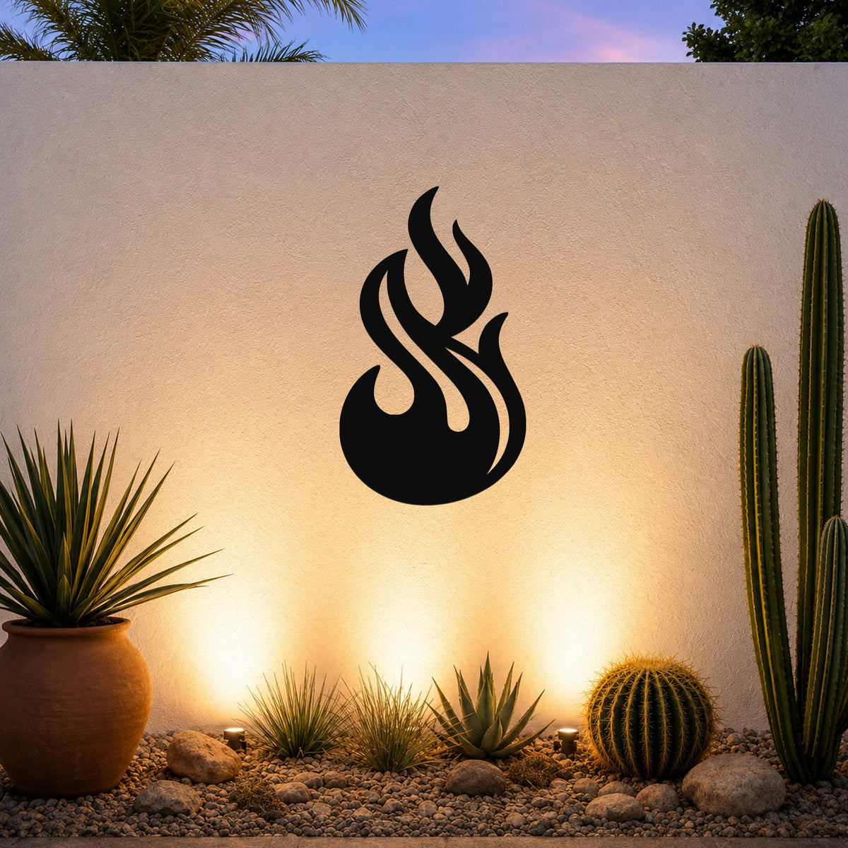 Black metal flame wall art with fluid, cutout design, mounted on an outdoor wall above a desert garden with cacti and warm uplighting.