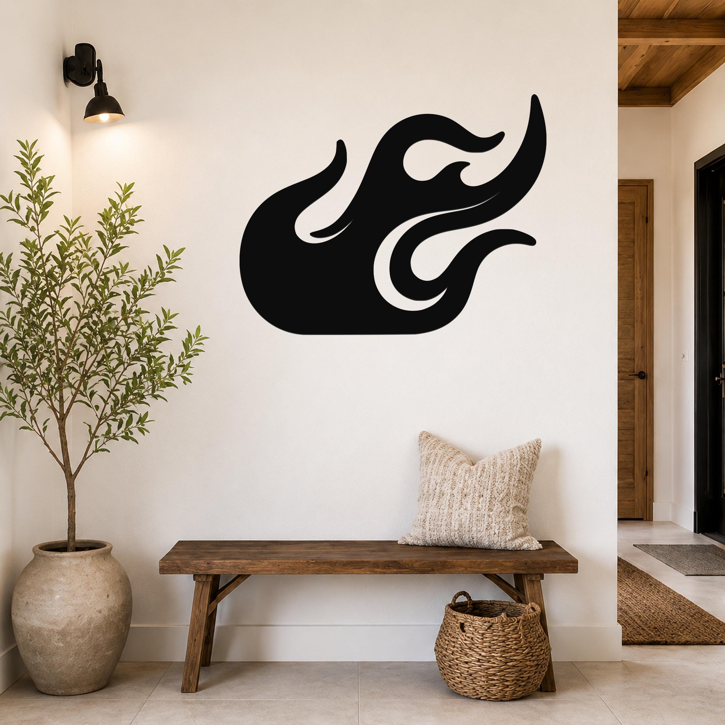 Black metal flame wall art with flowing cutout design, mounted on a white wall above a wooden bench in a modern entryway.
