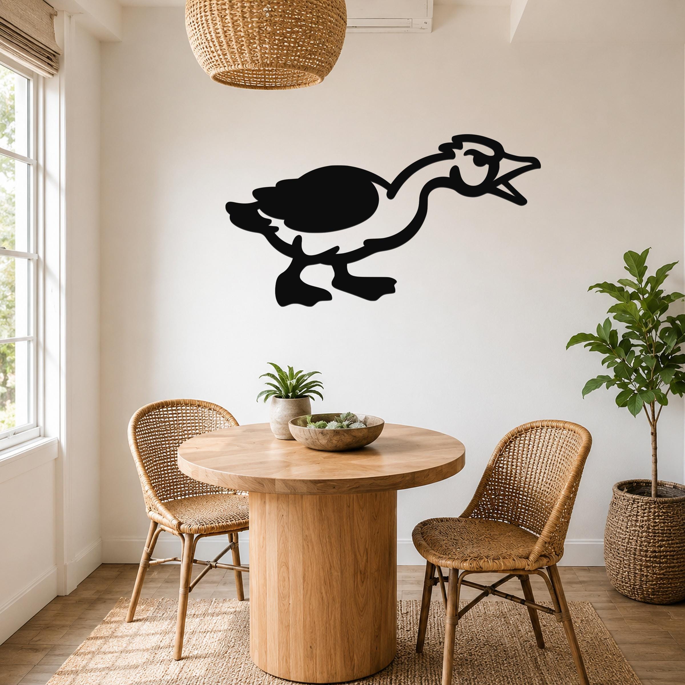 Black metal goose wall art silhouette with open beak and extended neck, mounted on a white wall above a round wooden table in a dining area.