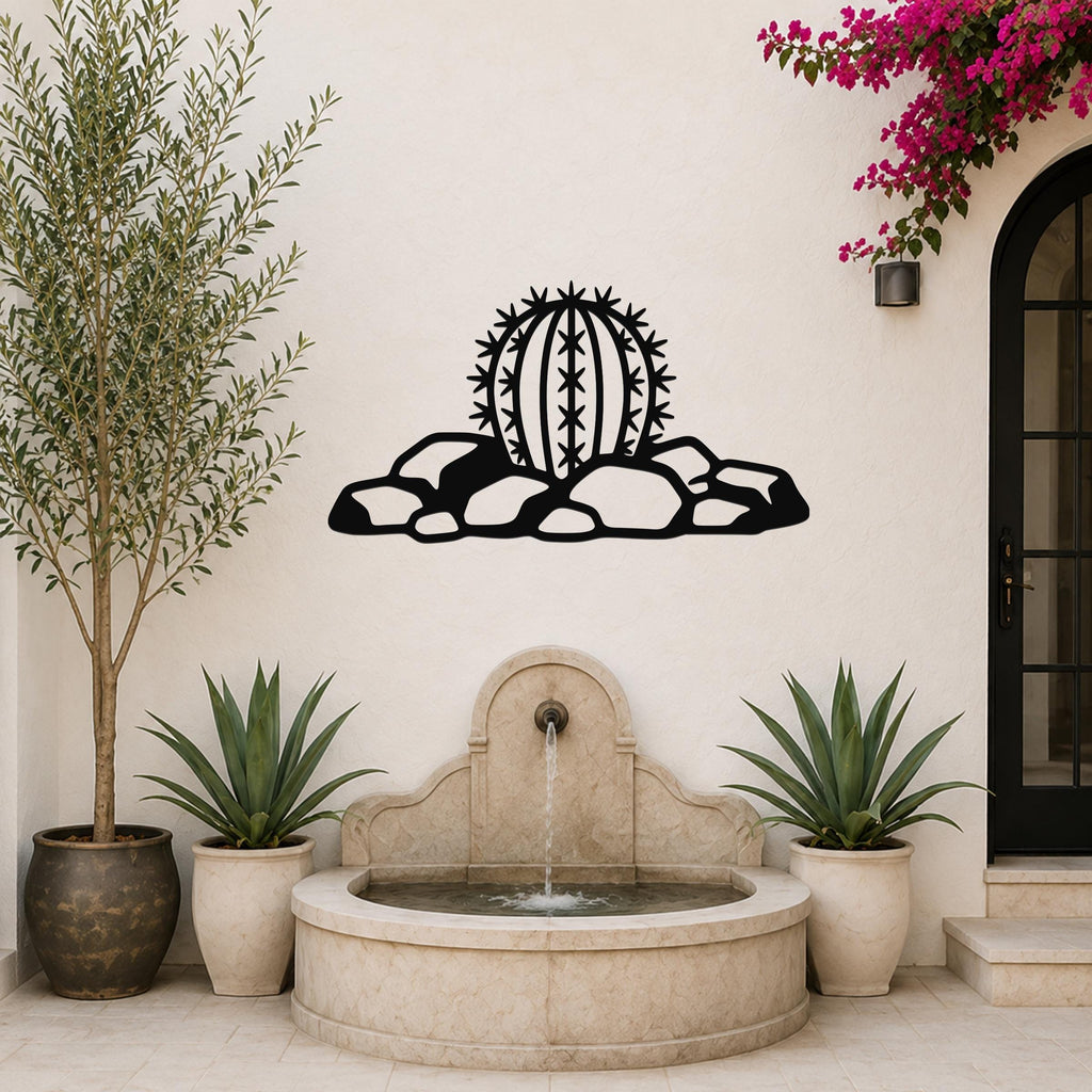 Black metal barrel cactus wall art with spines and rocks cutout, mounted on a white outdoor wall above a stone fountain.