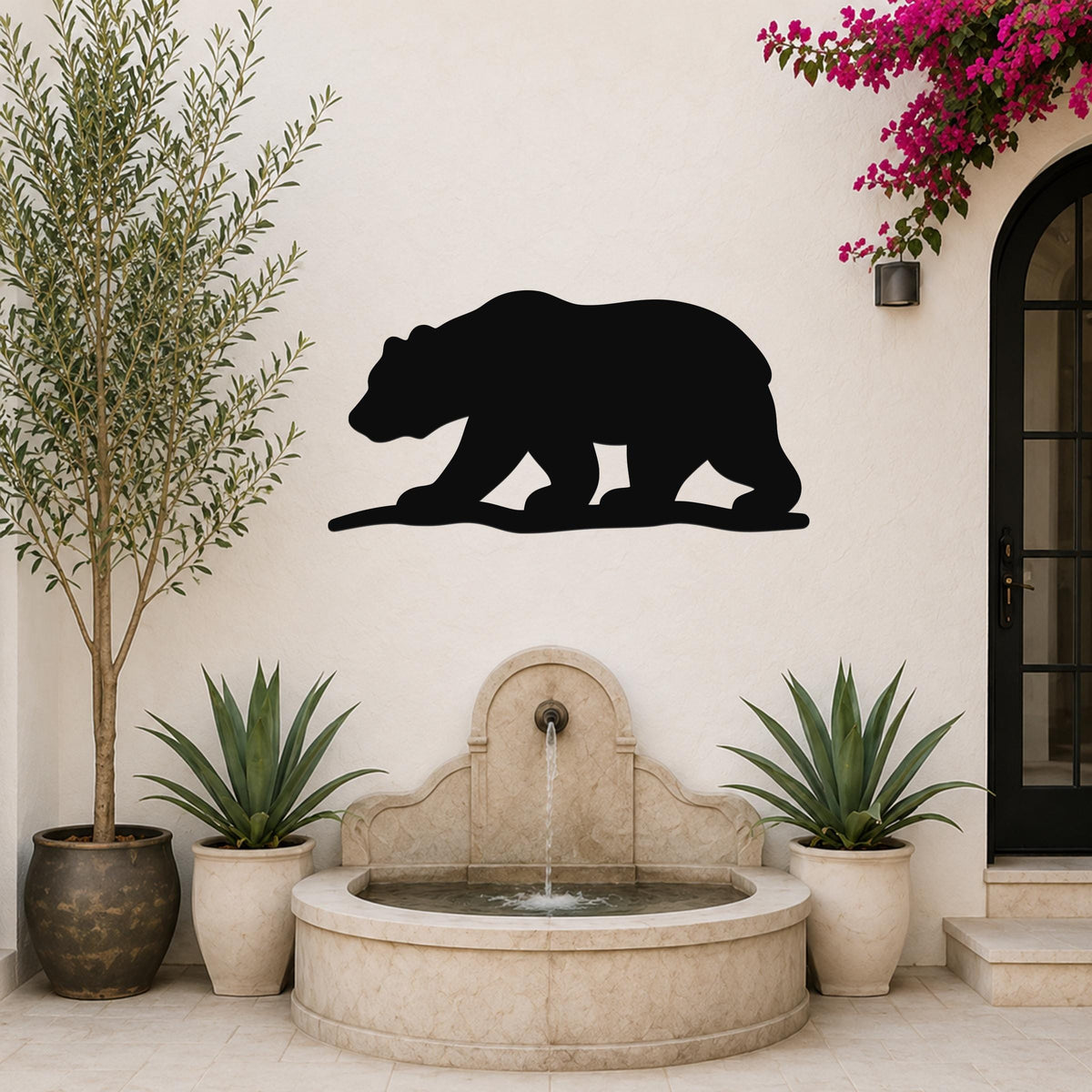 Black metal bear silhouette wall art mounted on a light-colored outdoor wall above a stone fountain, flanked by potted plants and a flowering vine.
