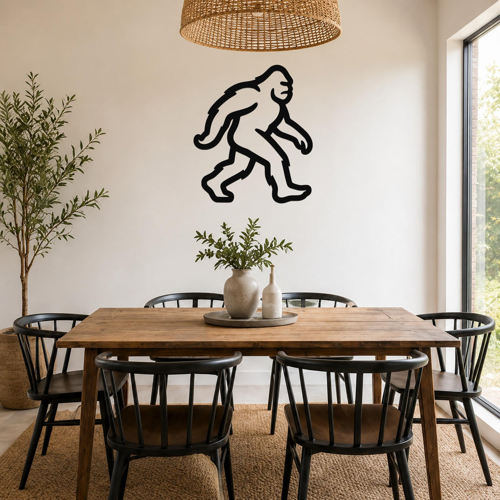 Black metal Bigfoot wall art silhouette mounted on a white wall above a wooden dining table in a bright, modern dining room.