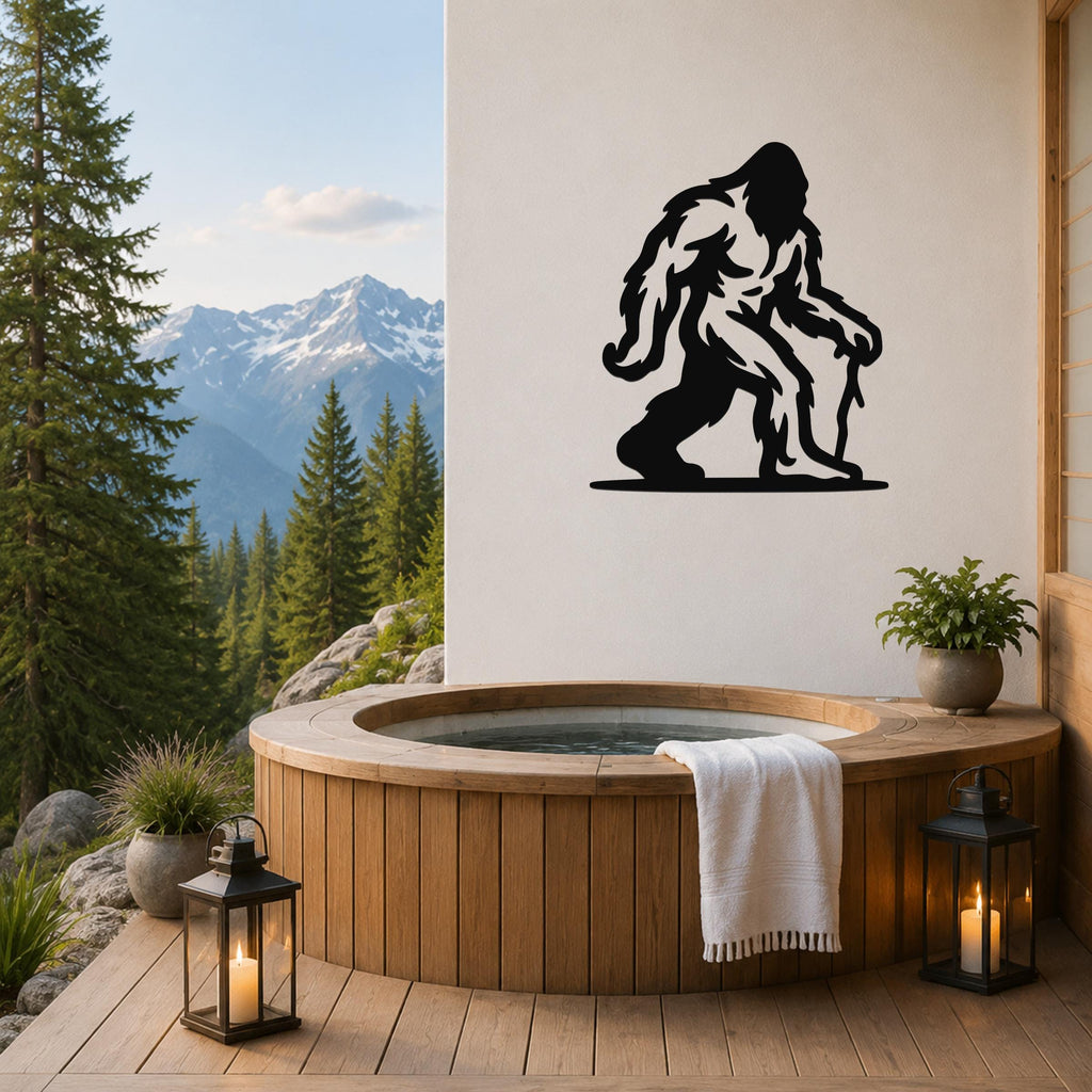 Black metal Bigfoot silhouette wall art mounted on a white wall above a wooden hot tub on a mountain-view deck.