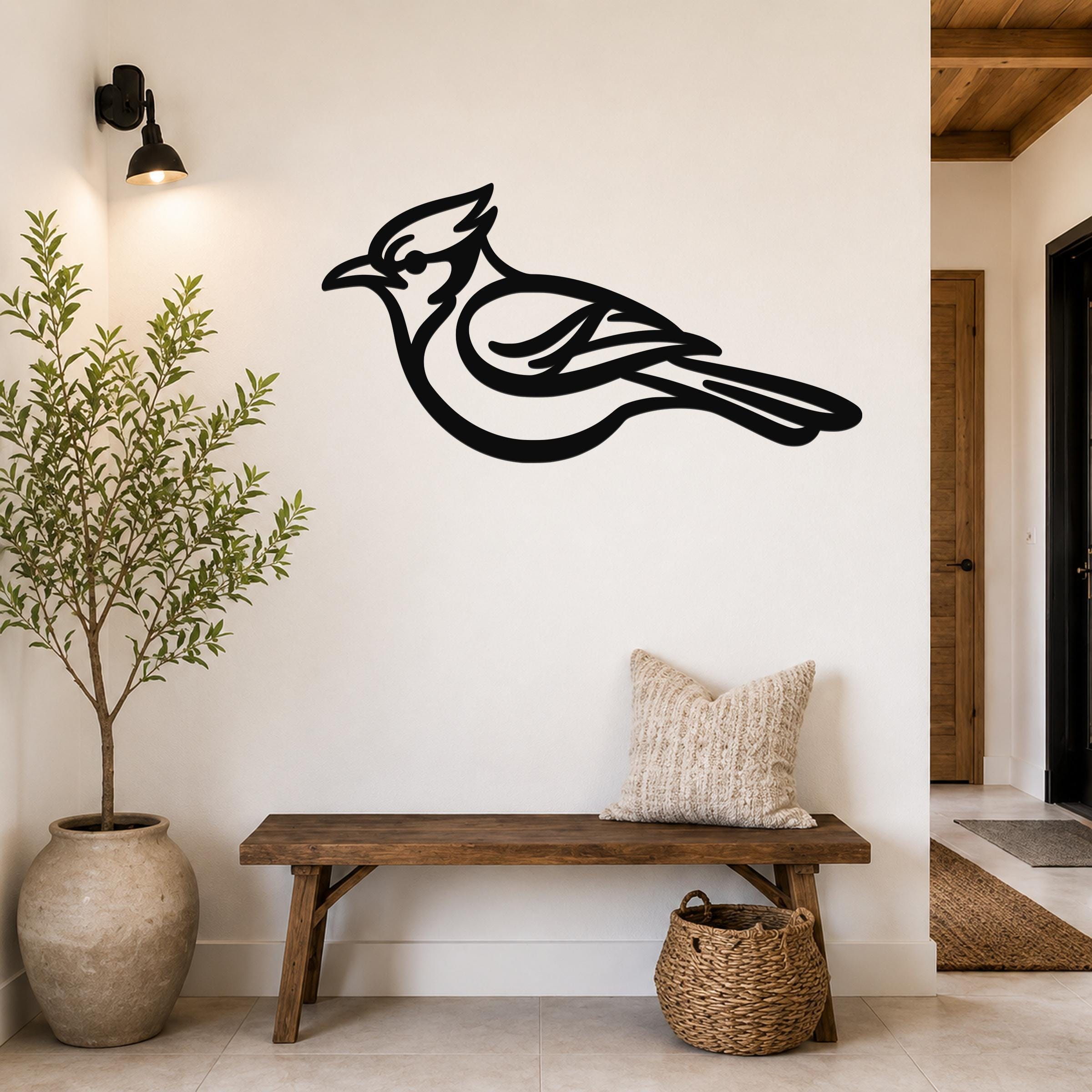 Black metal blue jay wall art silhouette mounted on a white wall above a wooden bench in a hallway.