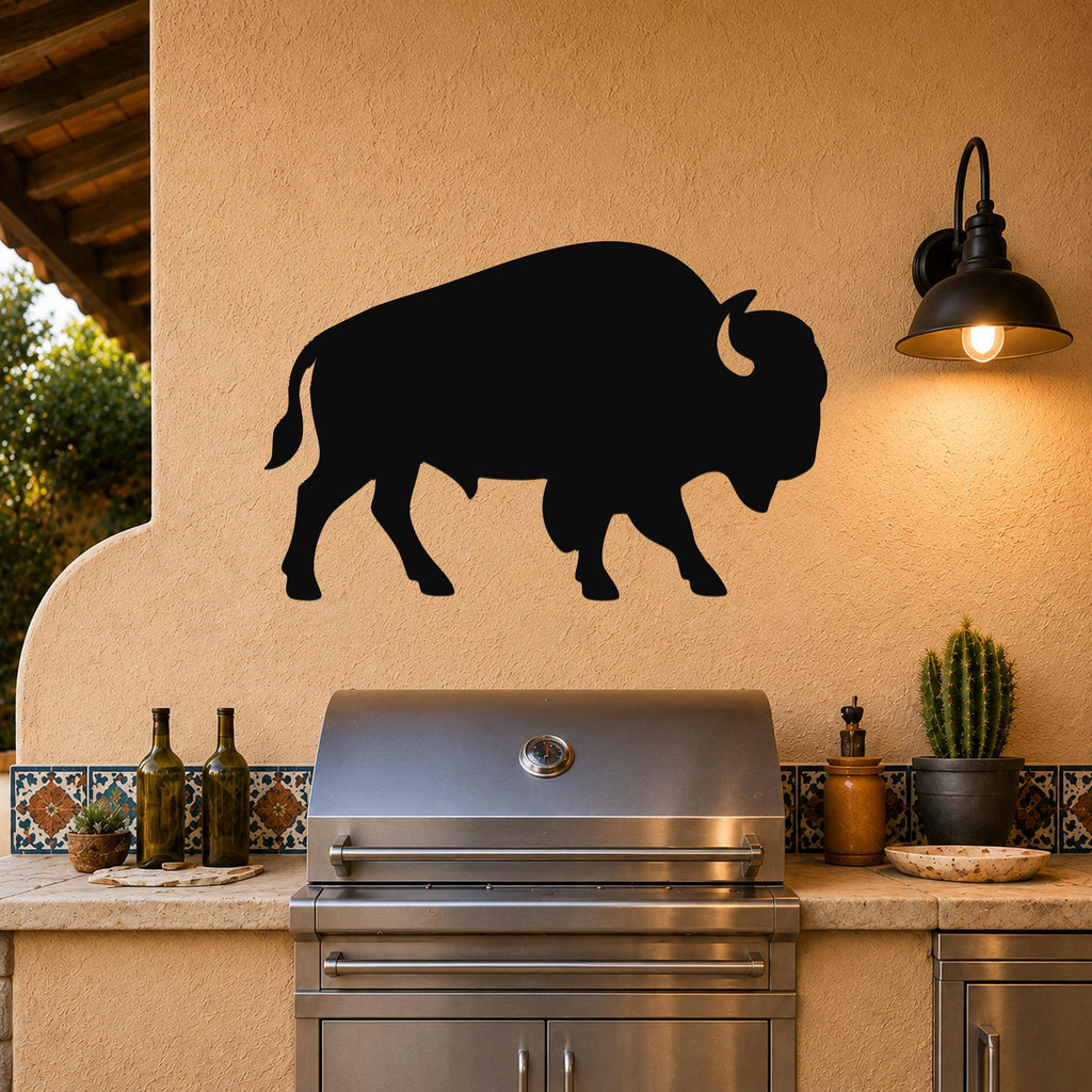 Black metal buffalo silhouette wall art mounted on a stucco wall above a stainless steel grill in an outdoor kitchen.