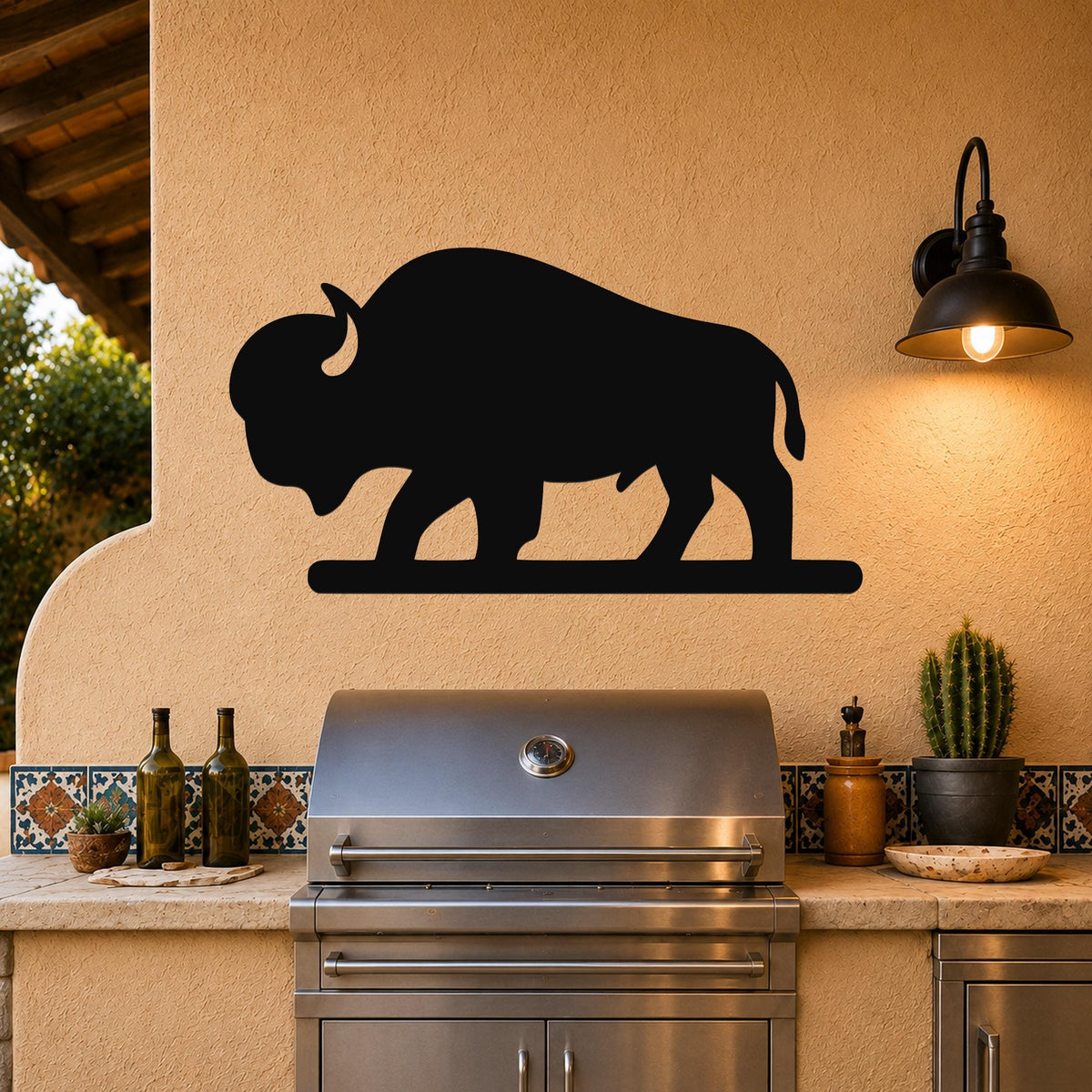Black metal bison silhouette wall art mounted on a stucco wall above a stainless steel grill in an outdoor kitchen.