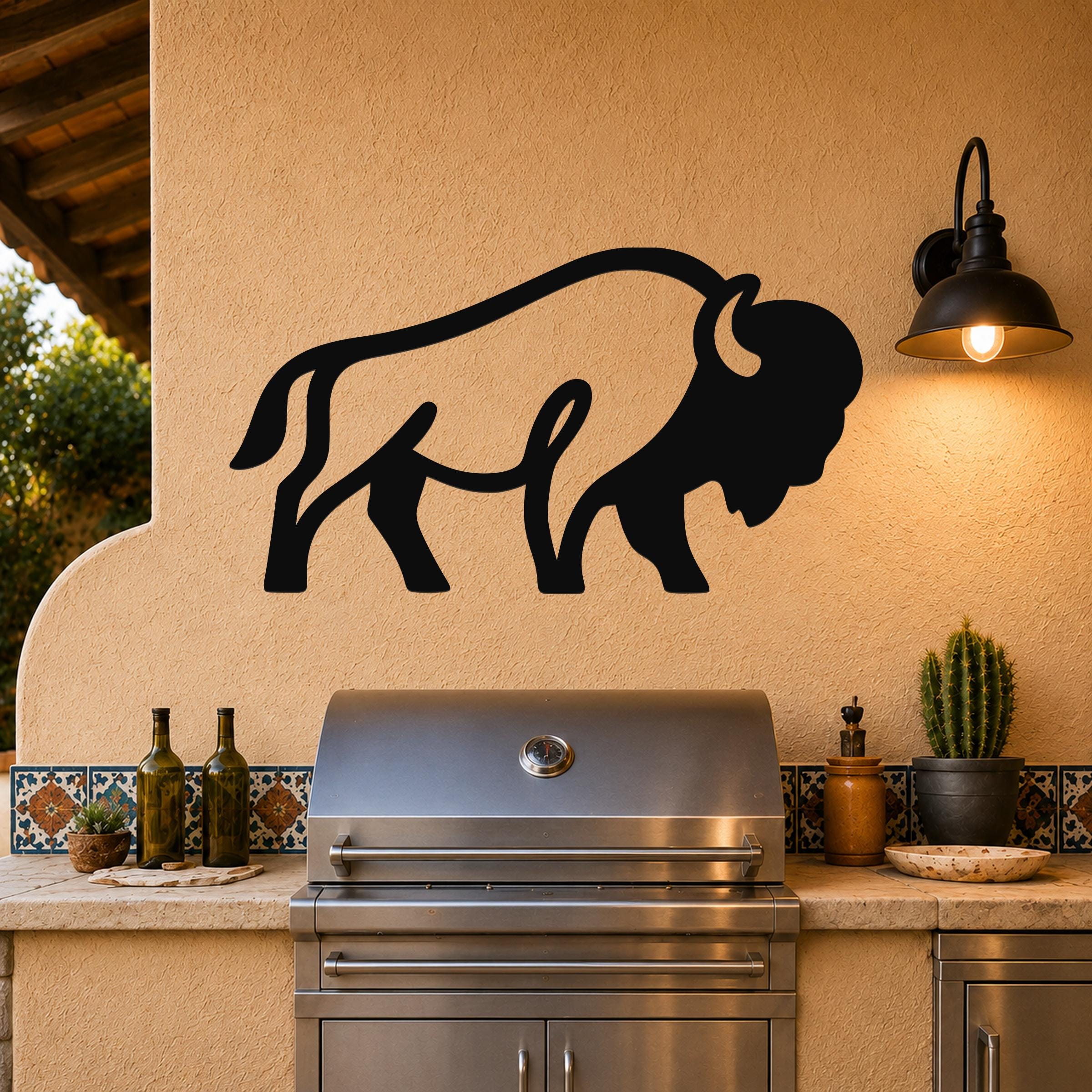 Black metal bison silhouette wall art mounted on a stucco wall above a stainless steel grill in an outdoor kitchen.