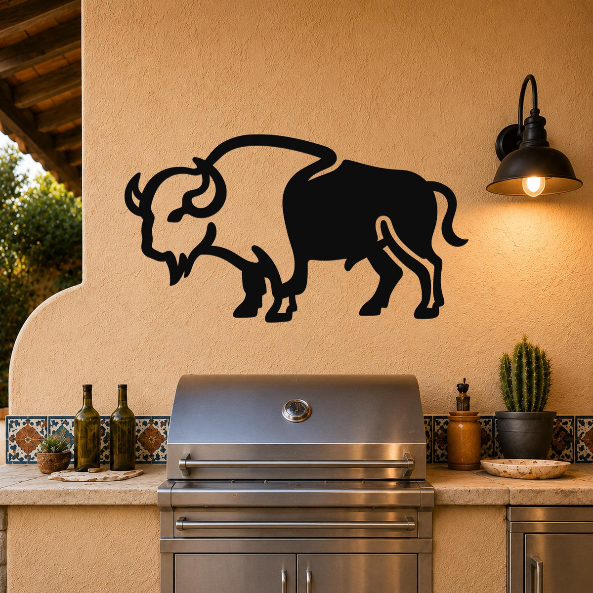 Black metal buffalo silhouette wall art mounted on a stucco wall above a stainless steel grill in an outdoor kitchen.