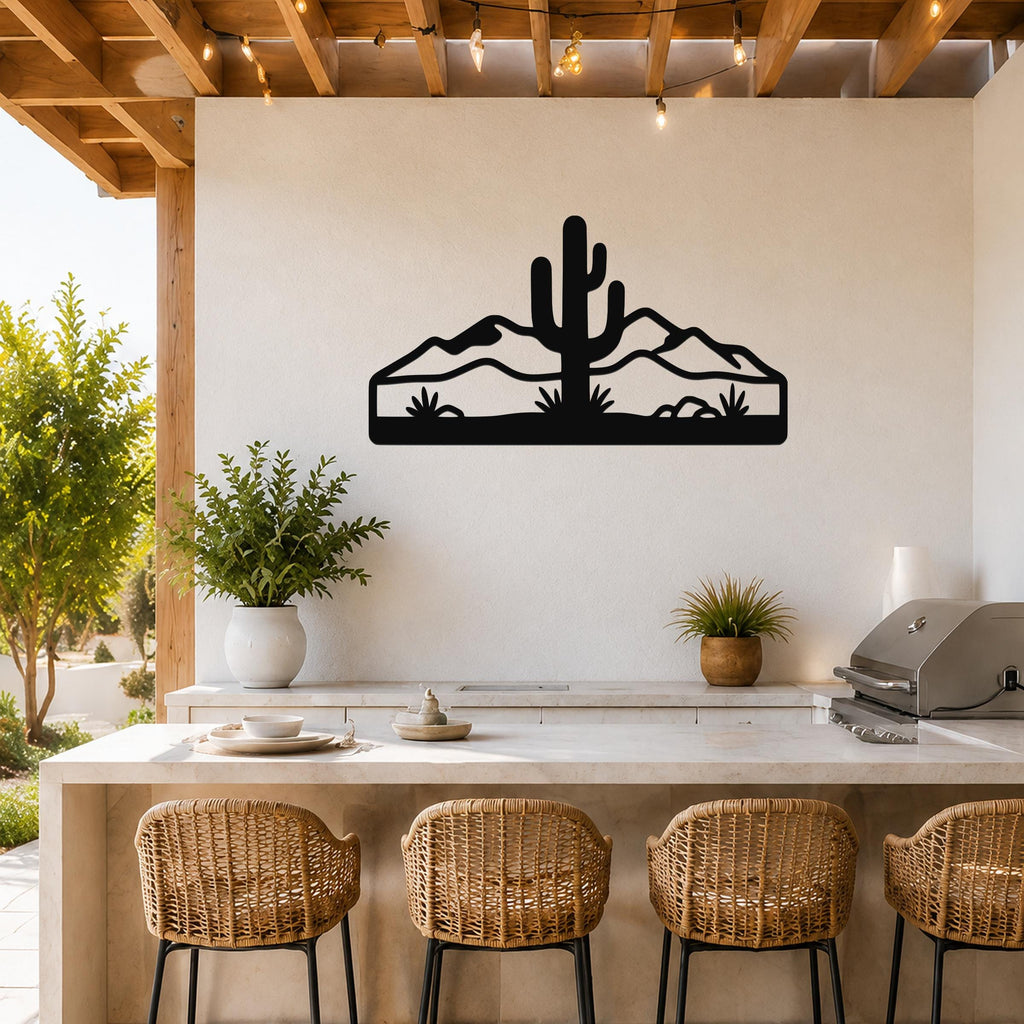 Black metal wall art silhouette of a saguaro cactus and desert mountains, mounted on a white wall above a kitchen counter with wicker bar stools.
