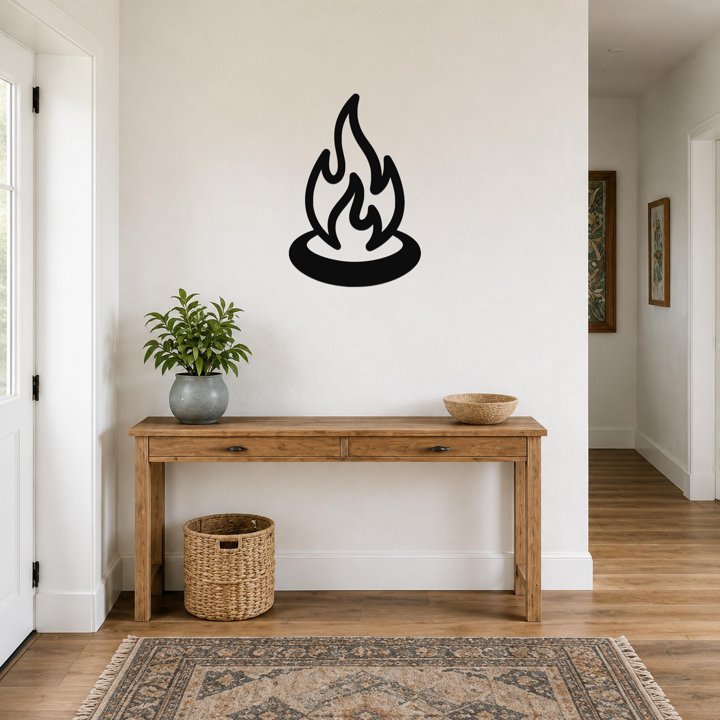 Black metal campfire wall art with flame silhouette, mounted on a white wall above a wooden console table in a hallway.