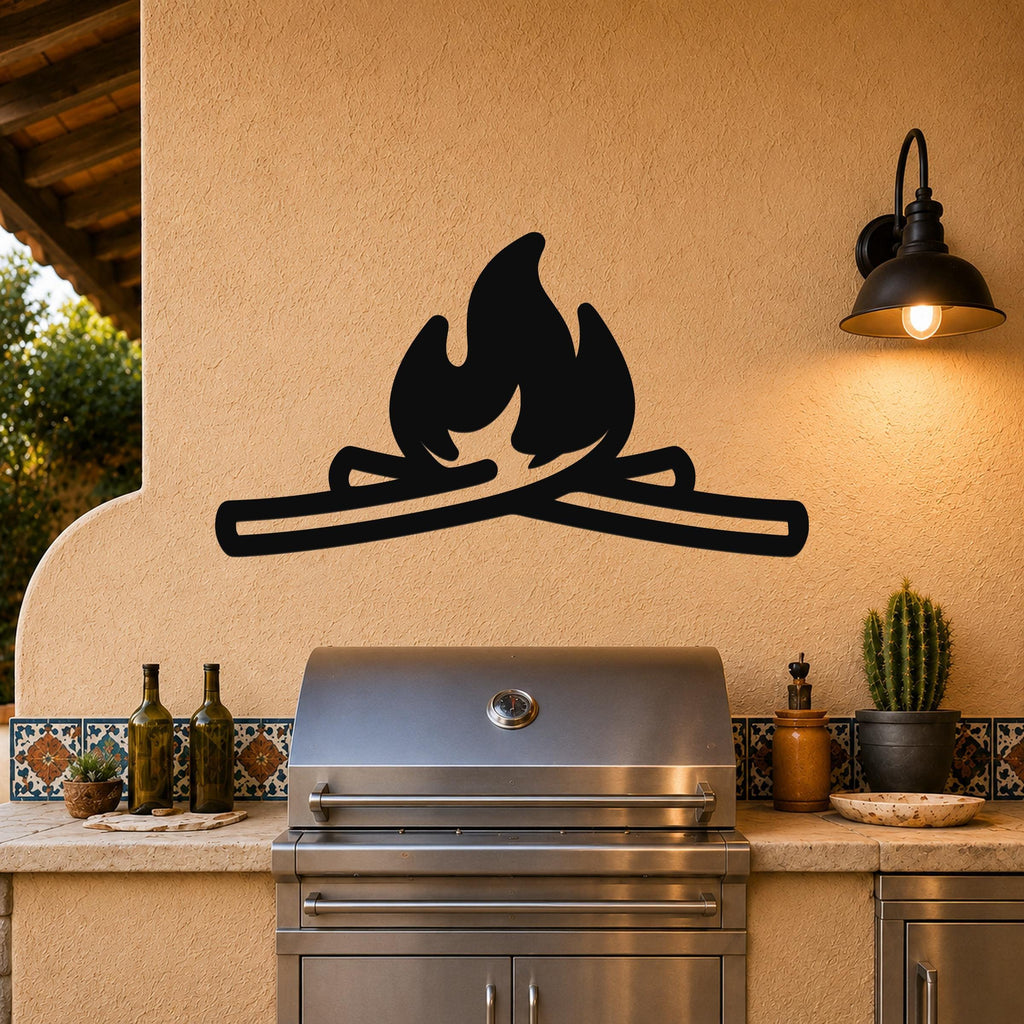 Black metal campfire wall art with flame and log silhouette, mounted on a stucco wall above a stainless steel grill on an outdoor patio.