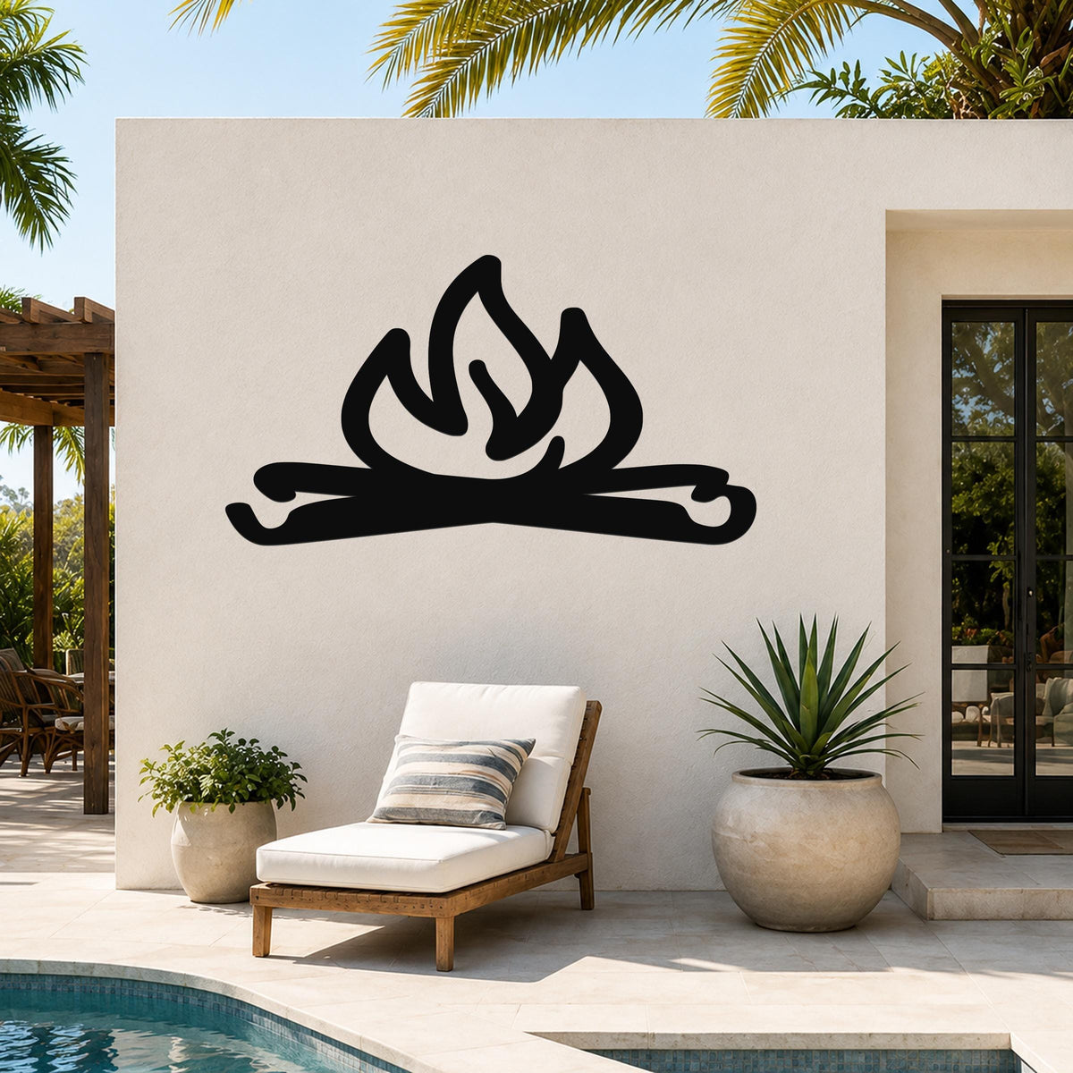 Black metal campfire wall art with flame and log cutouts, mounted on an outdoor patio wall above a lounge chair.