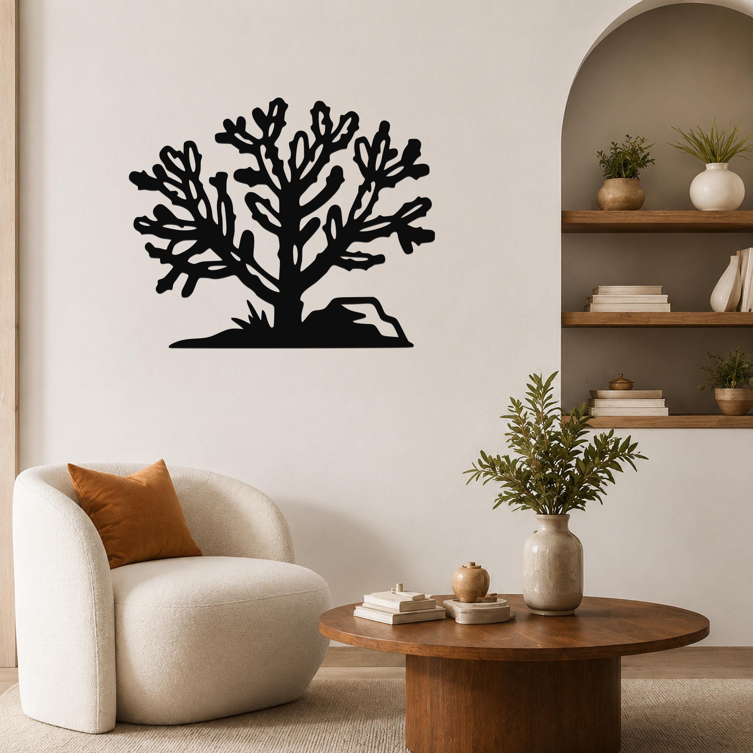 Black metal Cholla cactus wall art with branching cutouts, mounted on a living room wall above a white armchair.