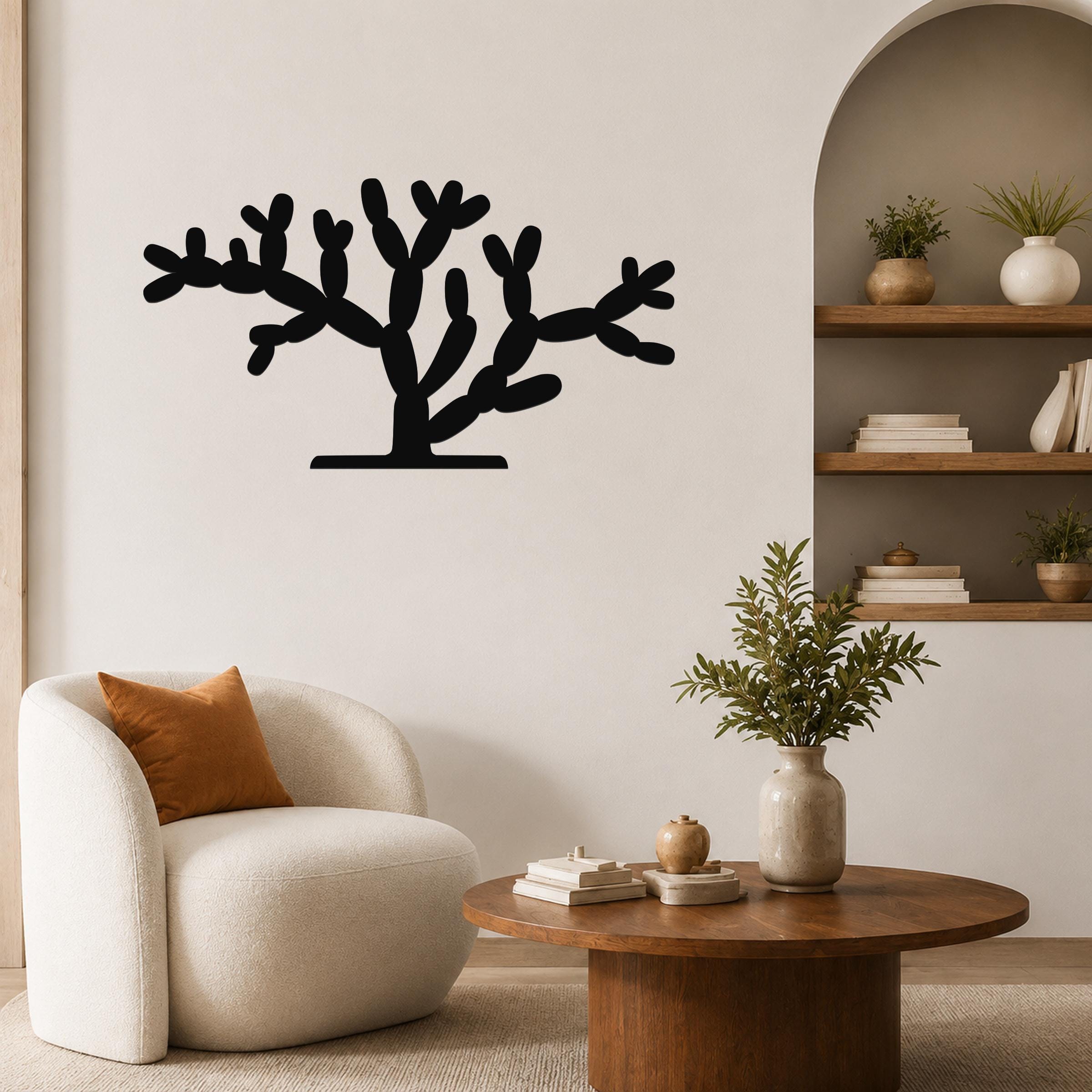 Black metal cholla cactus wall art with branching cutouts, mounted on a living room wall above a round wooden coffee table.