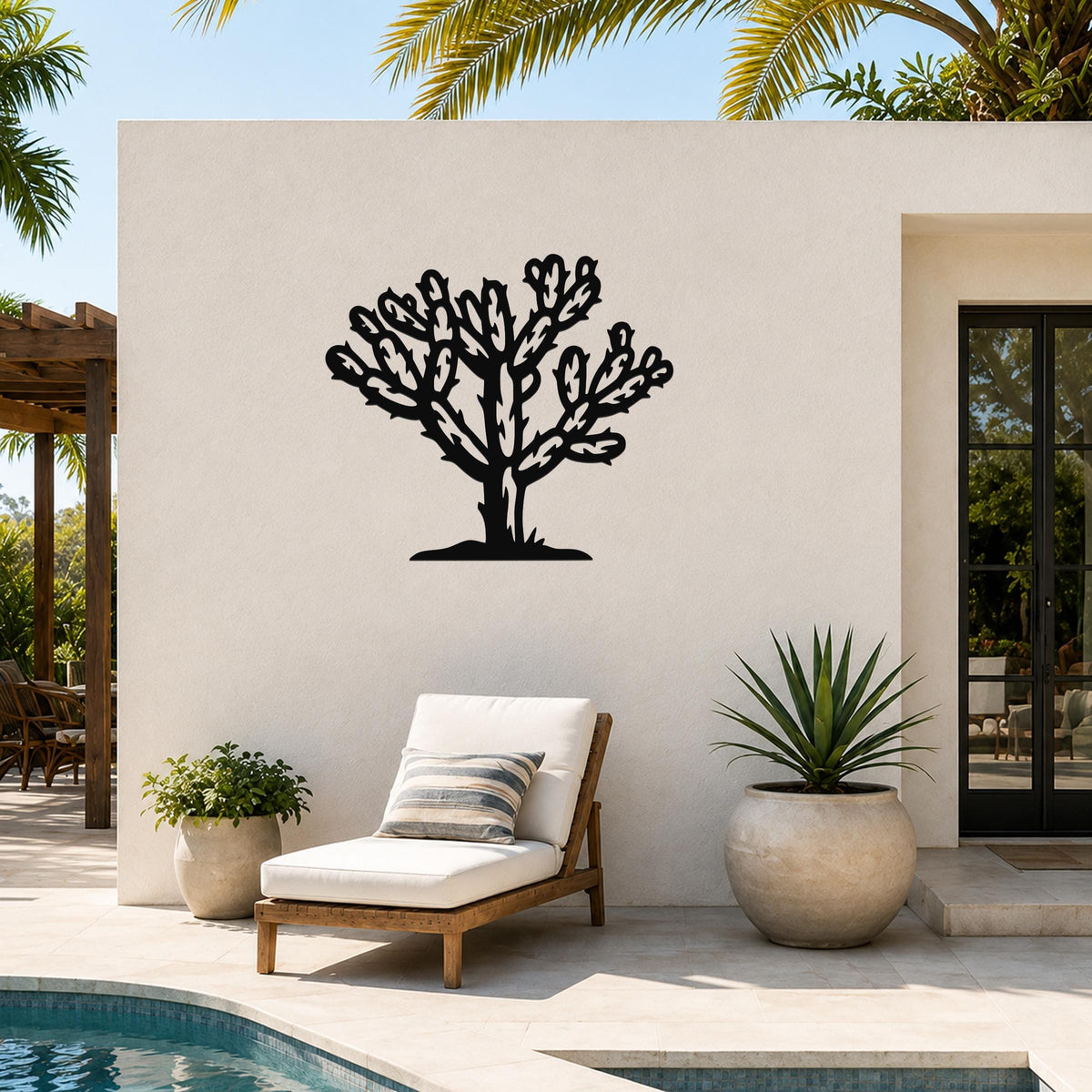 Black metal Cholla cactus wall art with detailed branch cutouts, mounted on a white outdoor wall beside a lounge chair and pool.