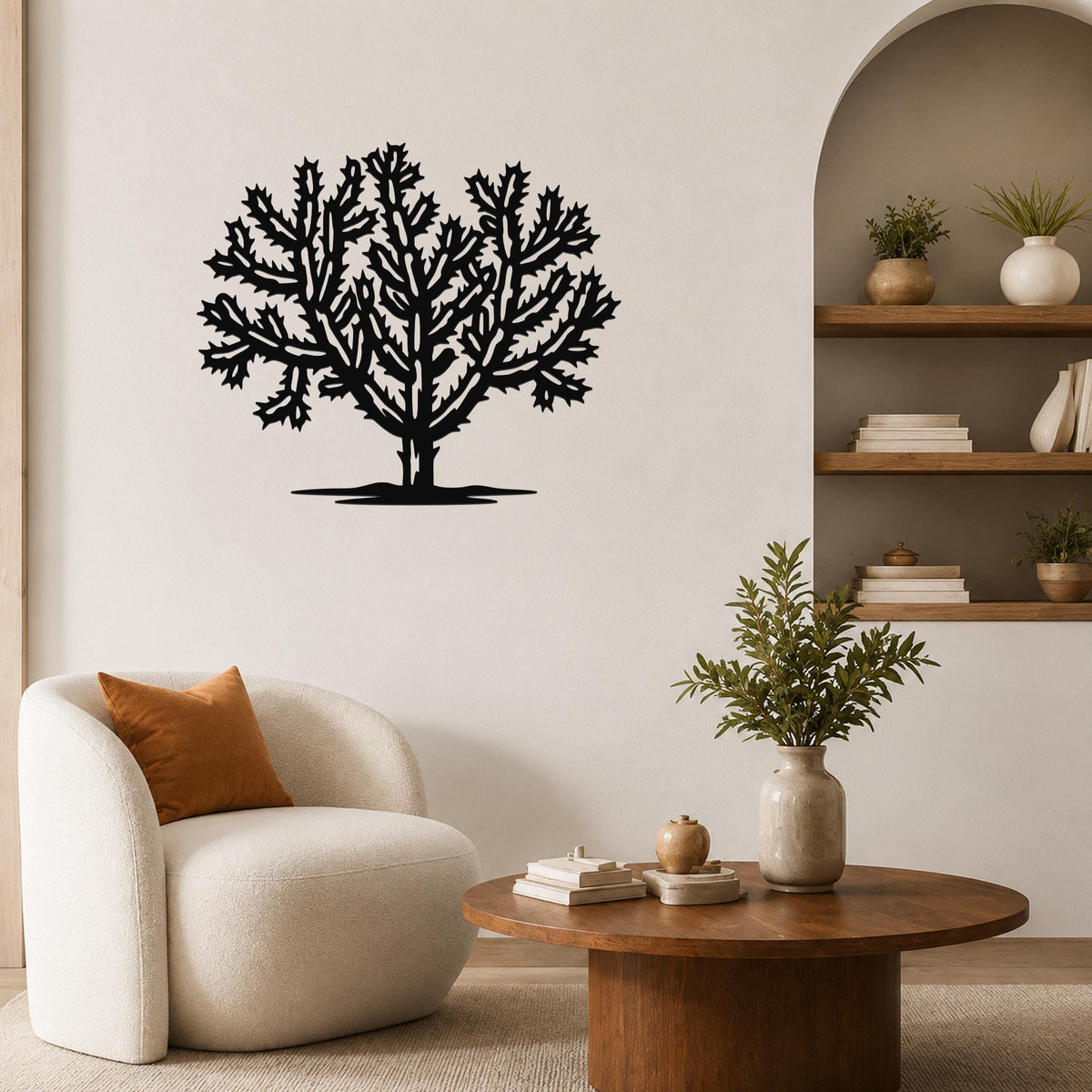 Black metal Cholla cactus wall art with intricate branching cutouts, mounted on a living room wall above a round wooden coffee table.