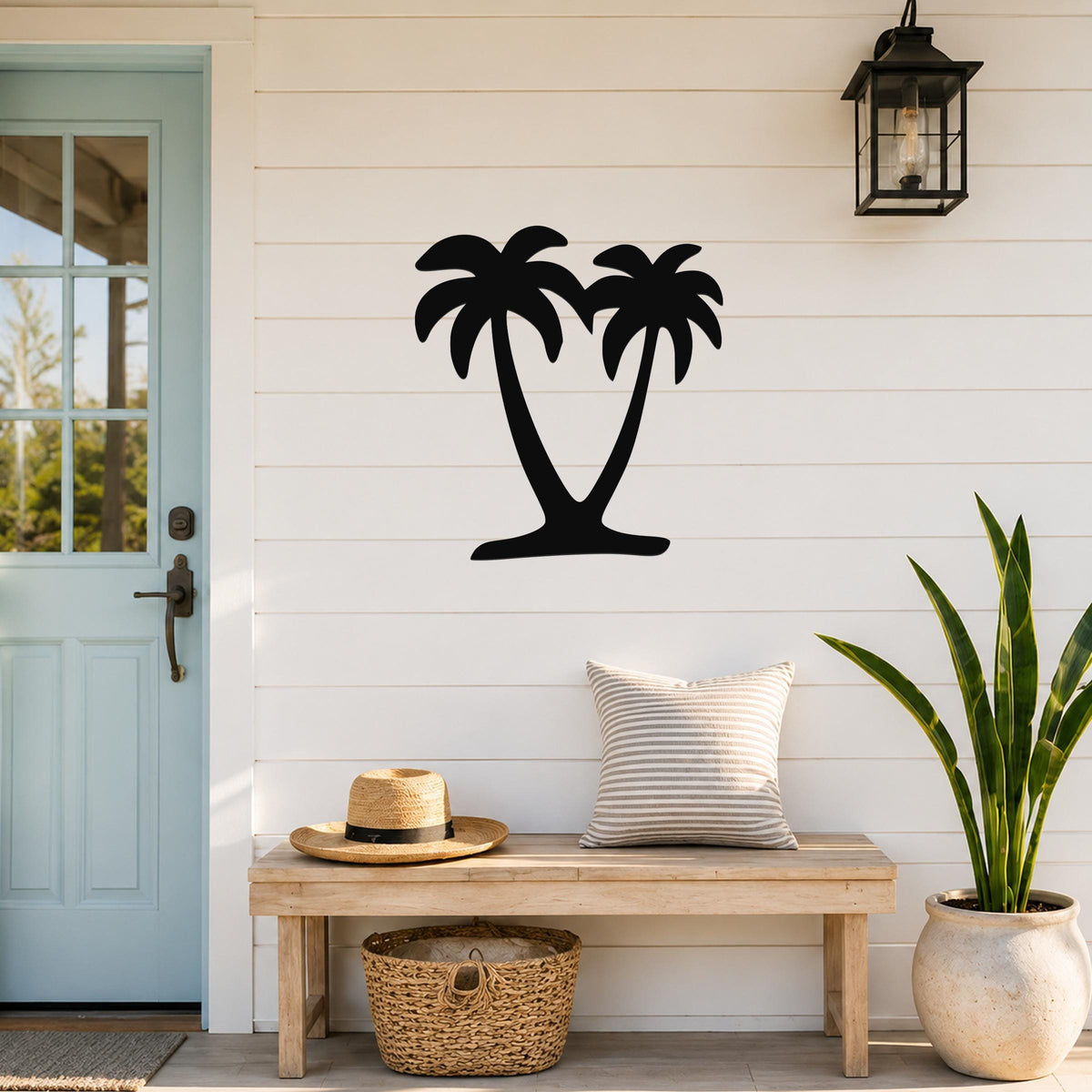 Black metal palm tree wall art with two silhouetted trees, mounted on a white shiplap wall above a wooden bench in a coastal entryway.