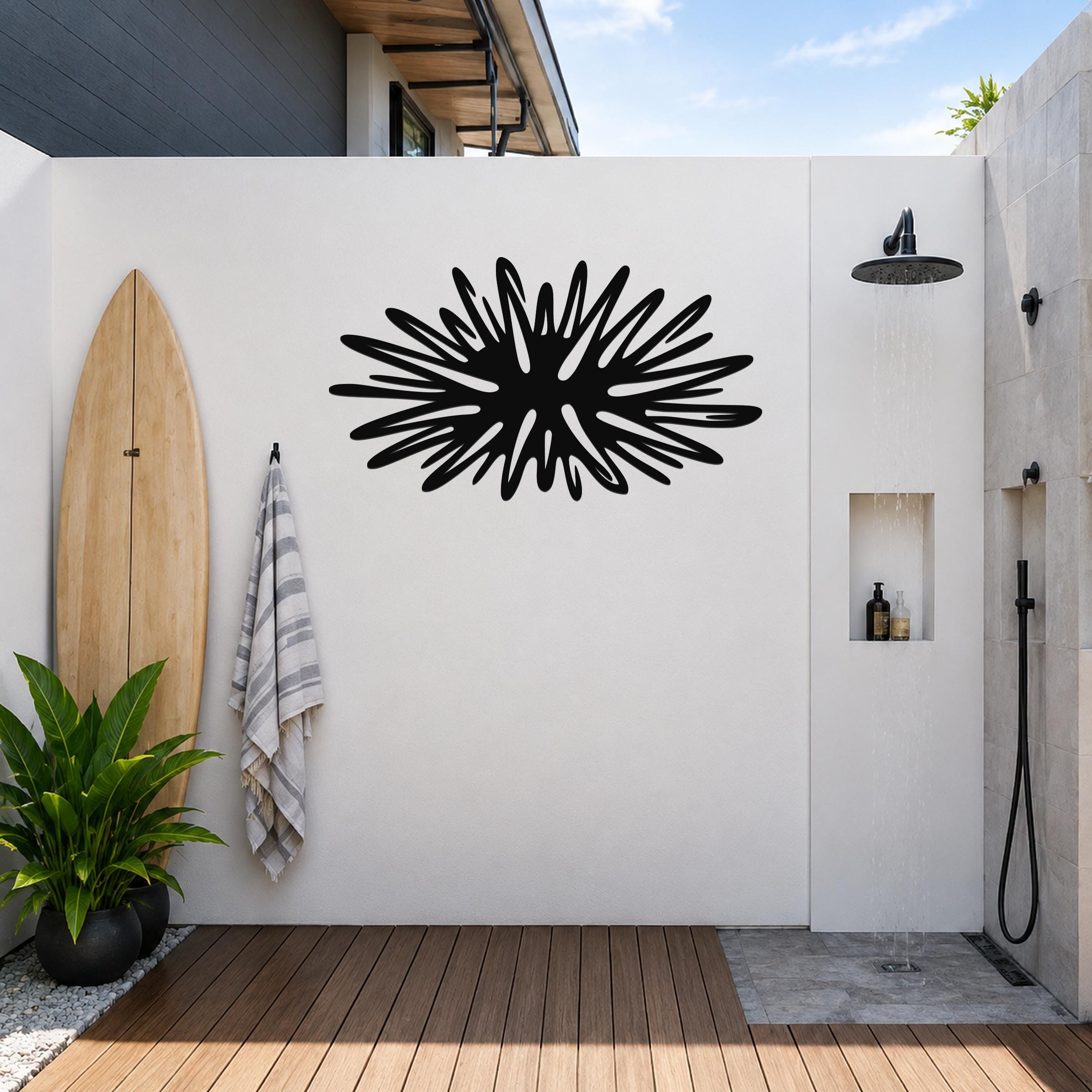 Black metal sea urchin wall art with spiky radial cutouts, mounted on a white outdoor wall above a wooden deck near a shower area.