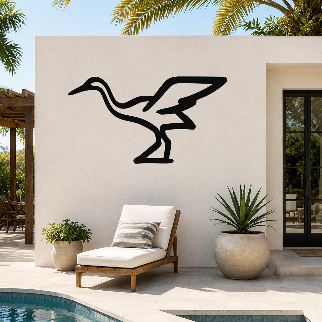 Black metal crane wall art silhouette mounted on an outdoor patio wall above a lounge chair, with palm trees and a pool in the background.