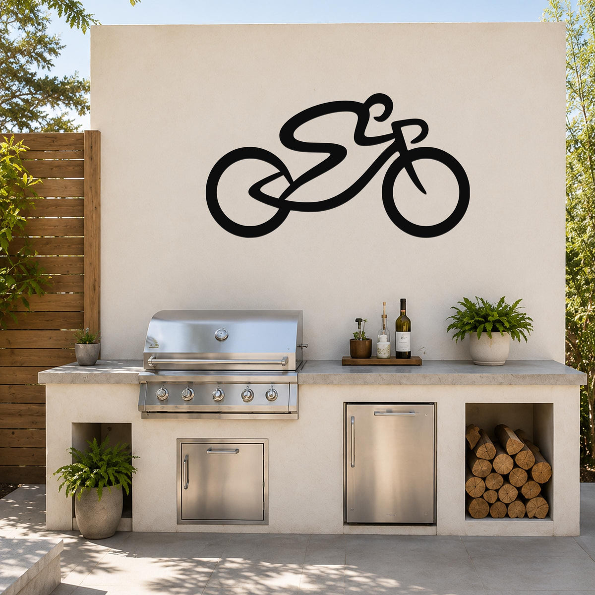 Black metal bicycle wall art with a bold silhouette design, mounted on an outdoor kitchen wall above a stainless steel grill and counter.