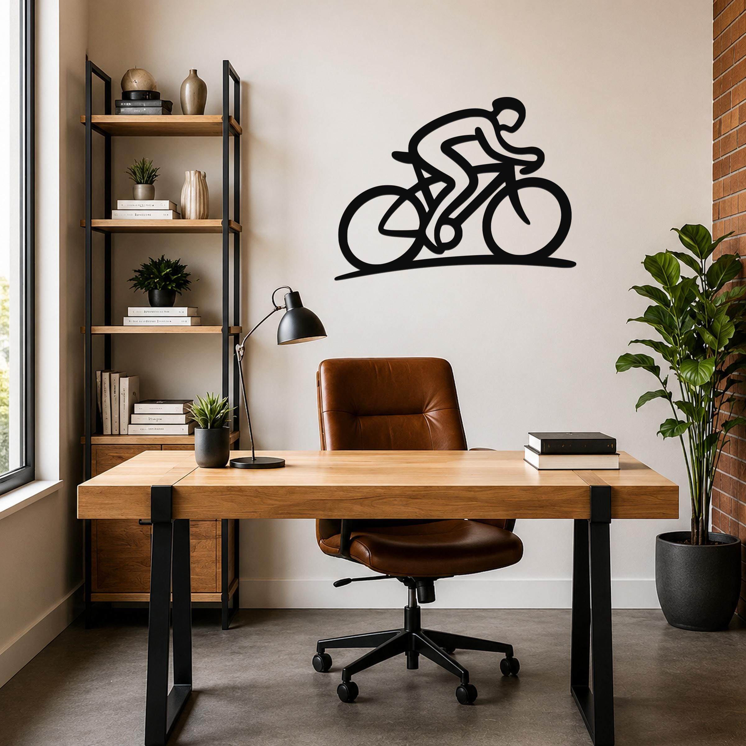 Black metal wall art featuring a cyclist silhouette in a dynamic riding pose, mounted on a wall above a wooden desk in a modern home office.