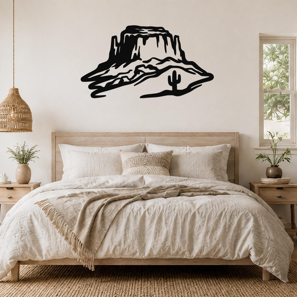 Black metal wall art silhouette of a desert mesa with a cactus, mounted above a bed in a neutral bedroom.