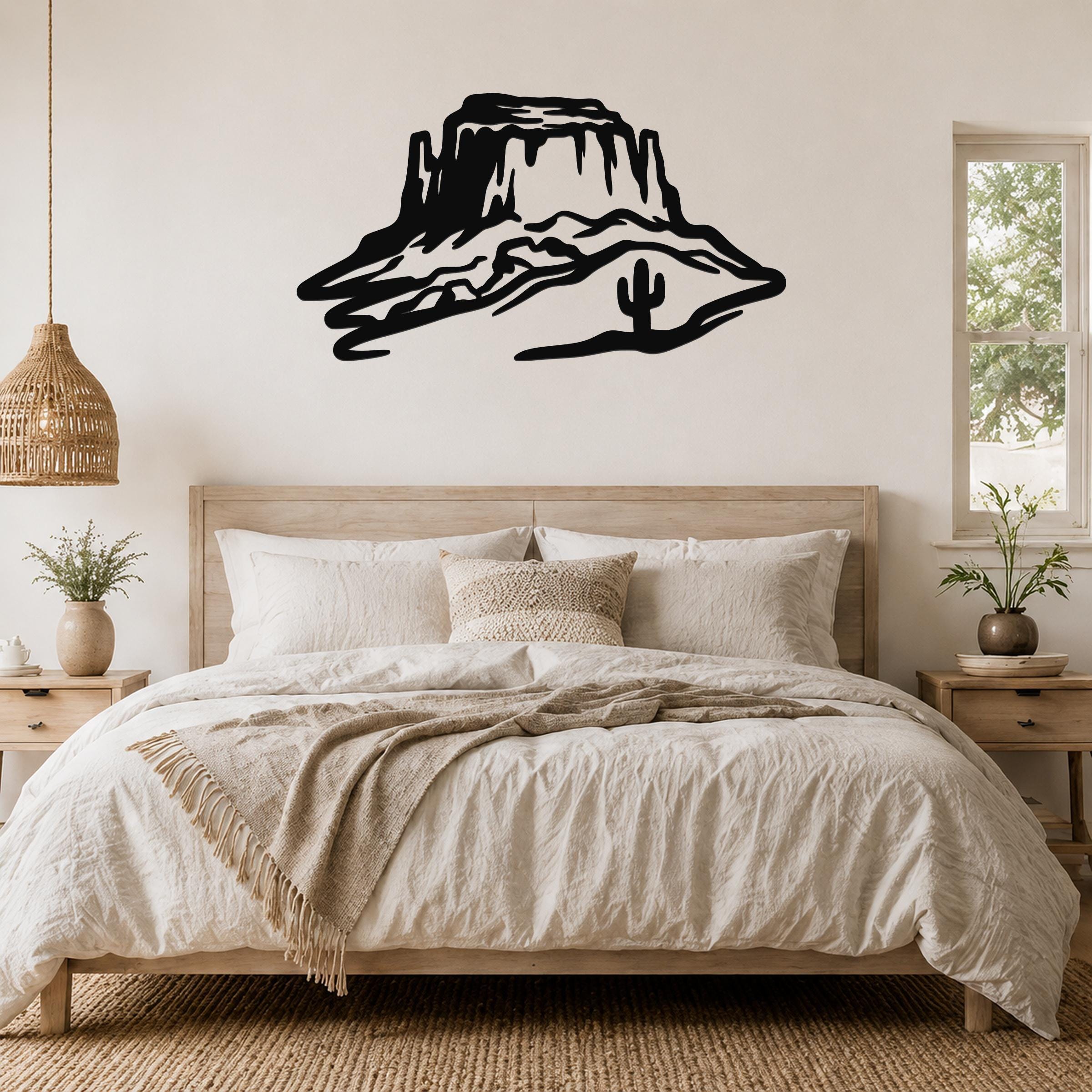 Black metal wall art silhouette of a desert mesa with a cactus, mounted above a bed in a neutral bedroom.