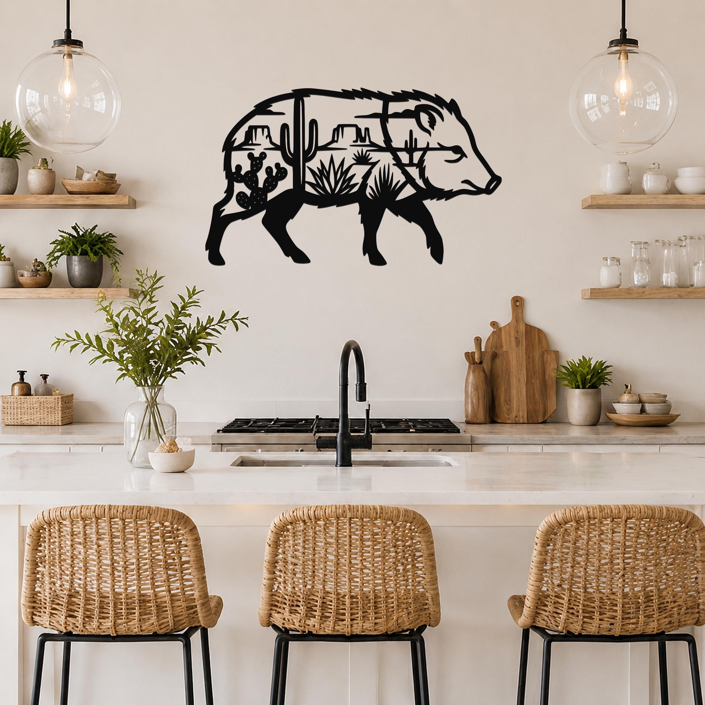 Black metal wall art in the silhouette of a javelina filled with desert cactus and mountain cutouts, mounted above a kitchen counter.