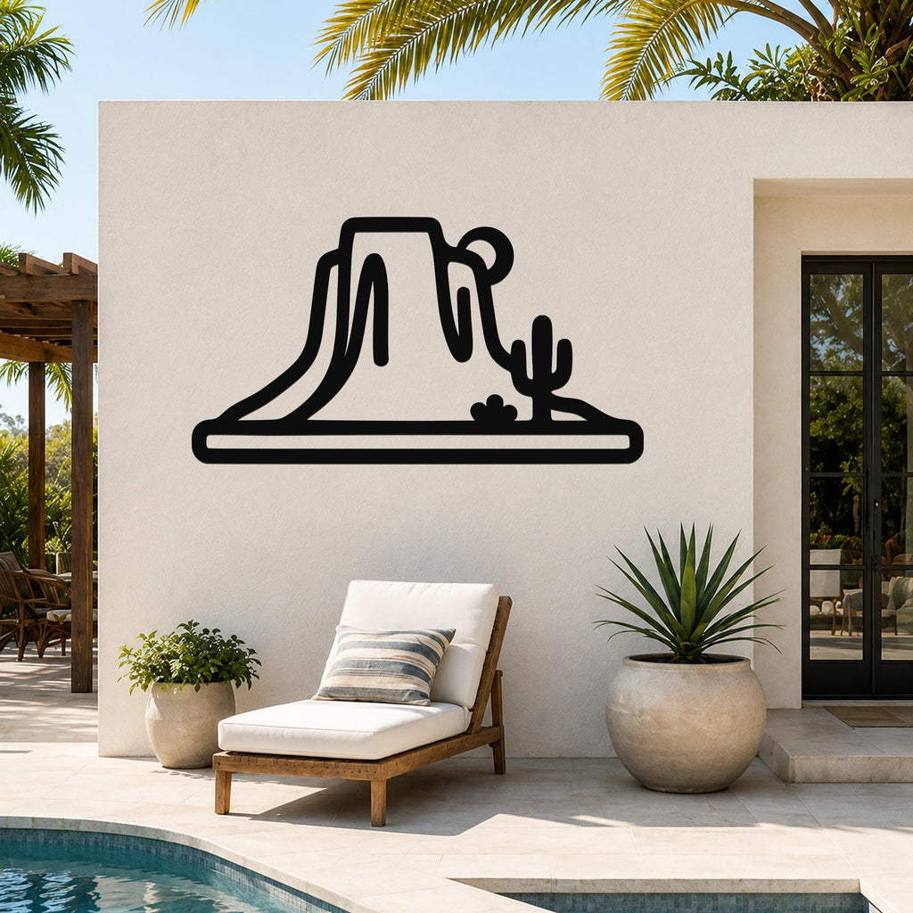 Black metal wall art silhouette of a desert mesa and cactus, mounted on an outdoor patio wall above a lounge chair.