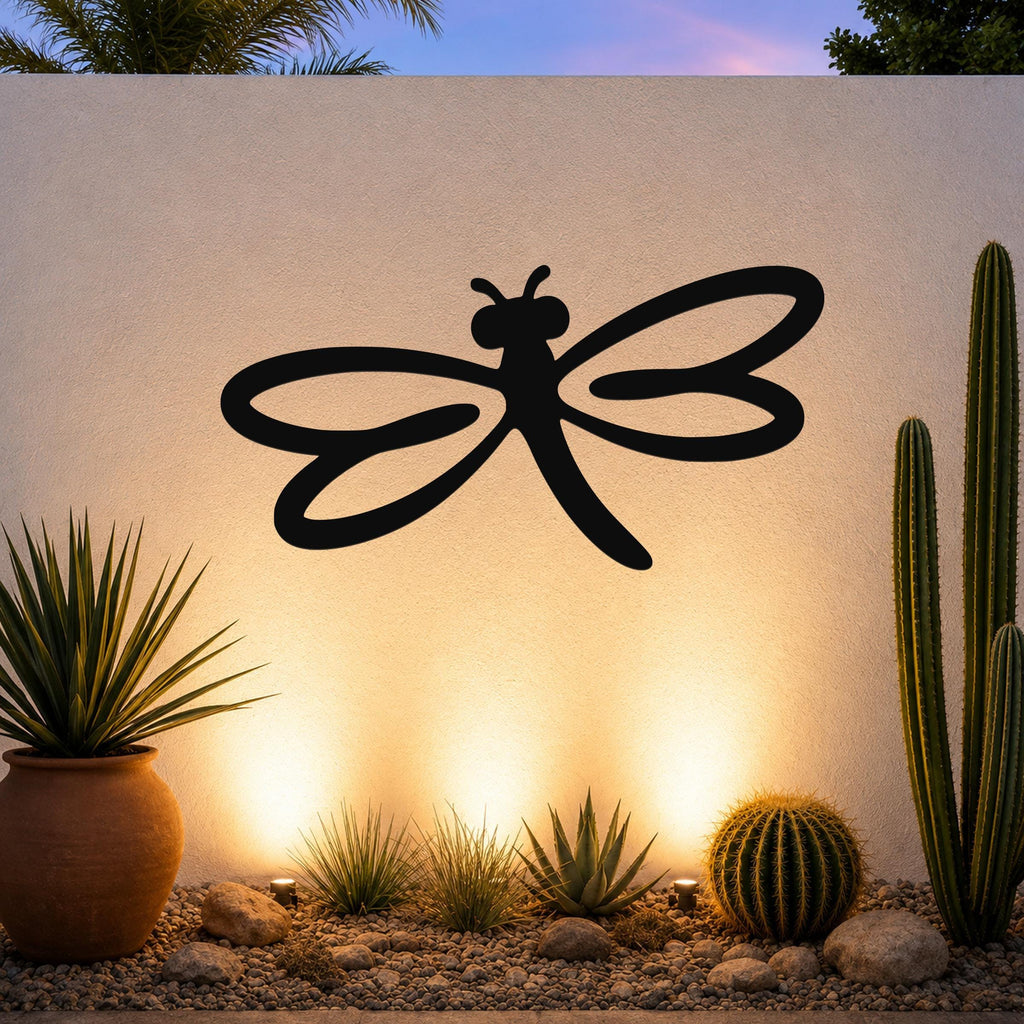Black metal dragonfly wall art with flowing wing cutouts, mounted on an outdoor wall above a desert garden with cacti and warm uplighting.